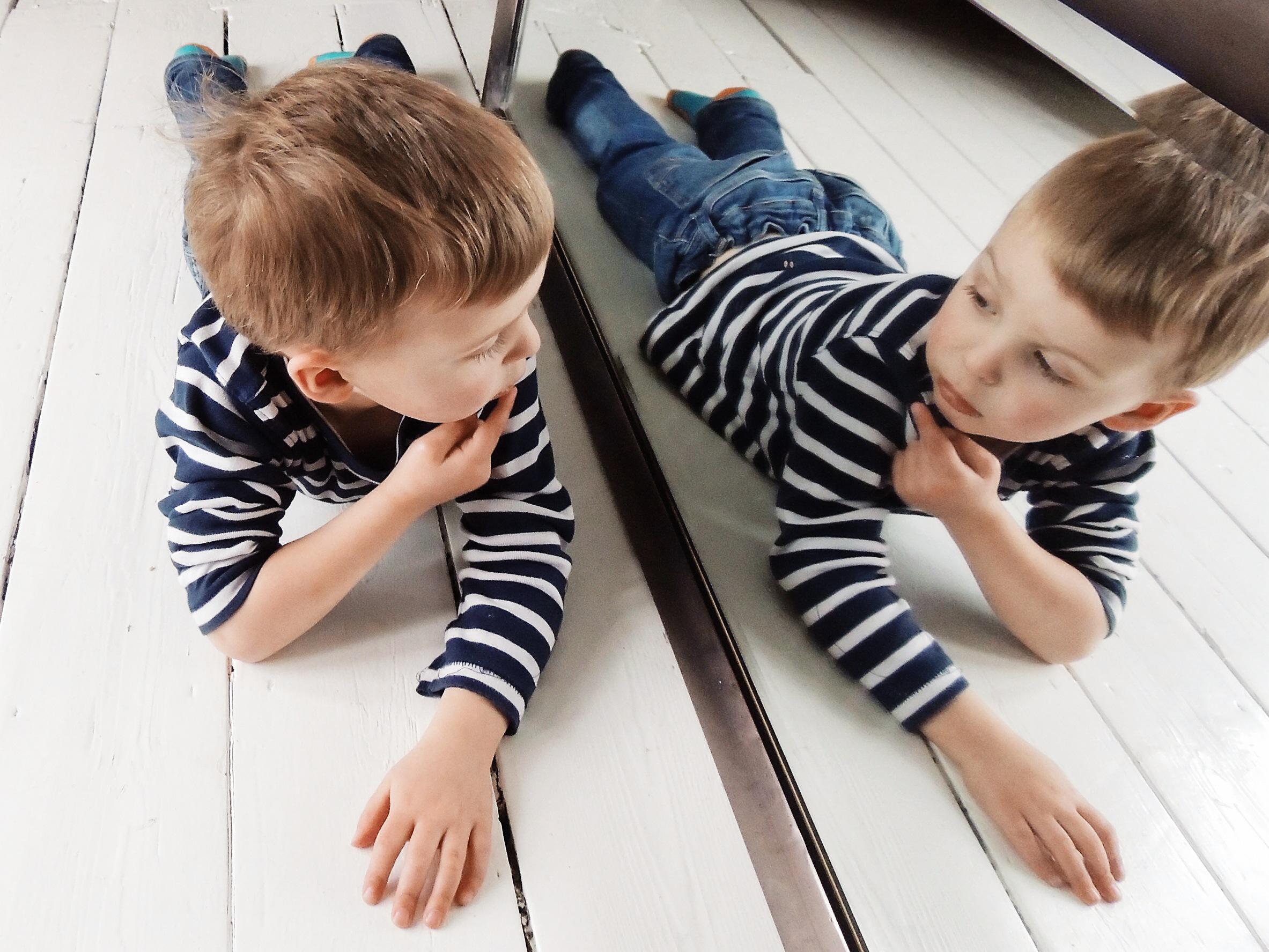 Portrait of a Boy lying on the floor looking at himself in the mirror