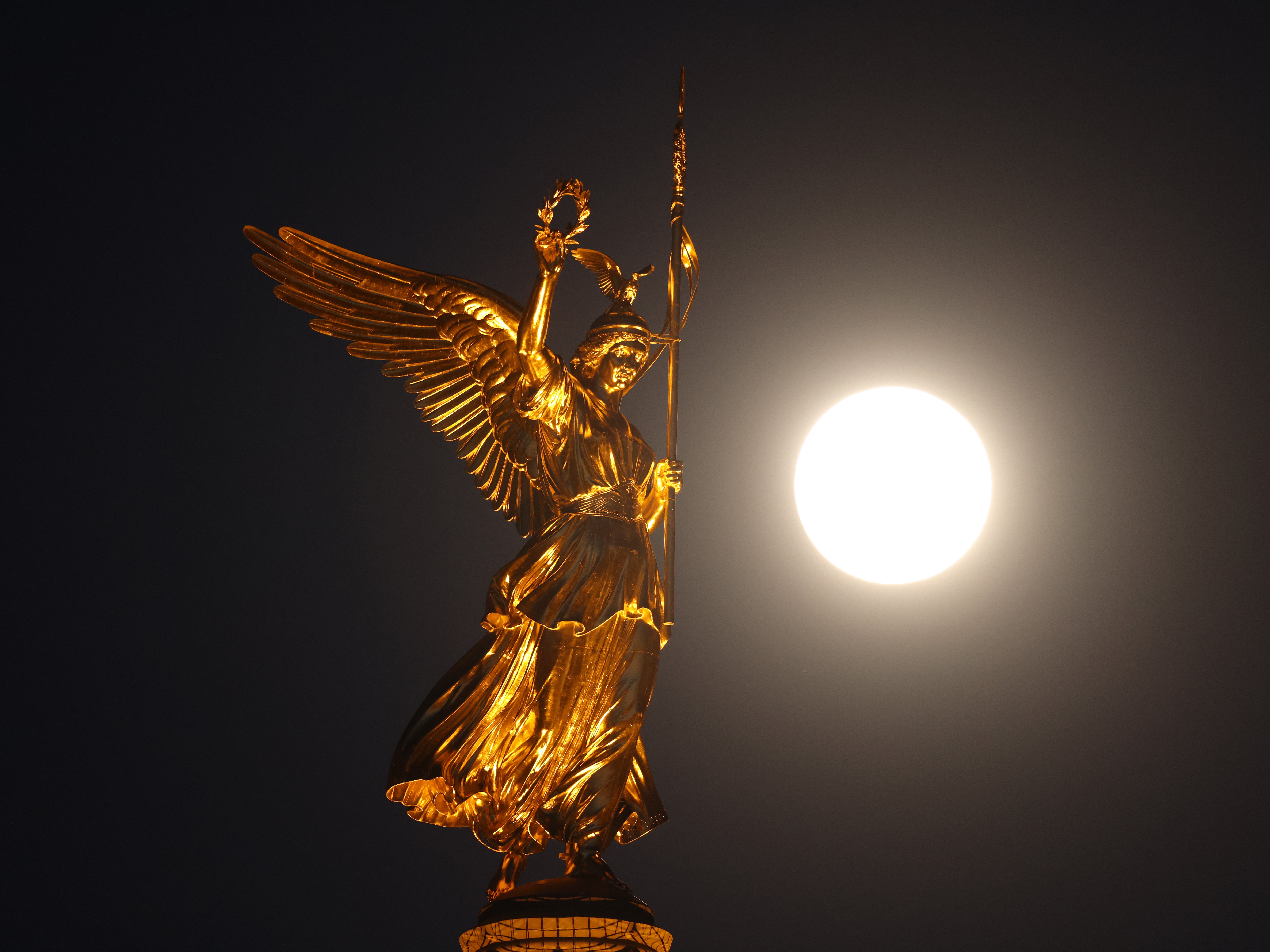 A supermoon shines next to the statue of Victoria on top of the Victory Column in Berlin, Germany