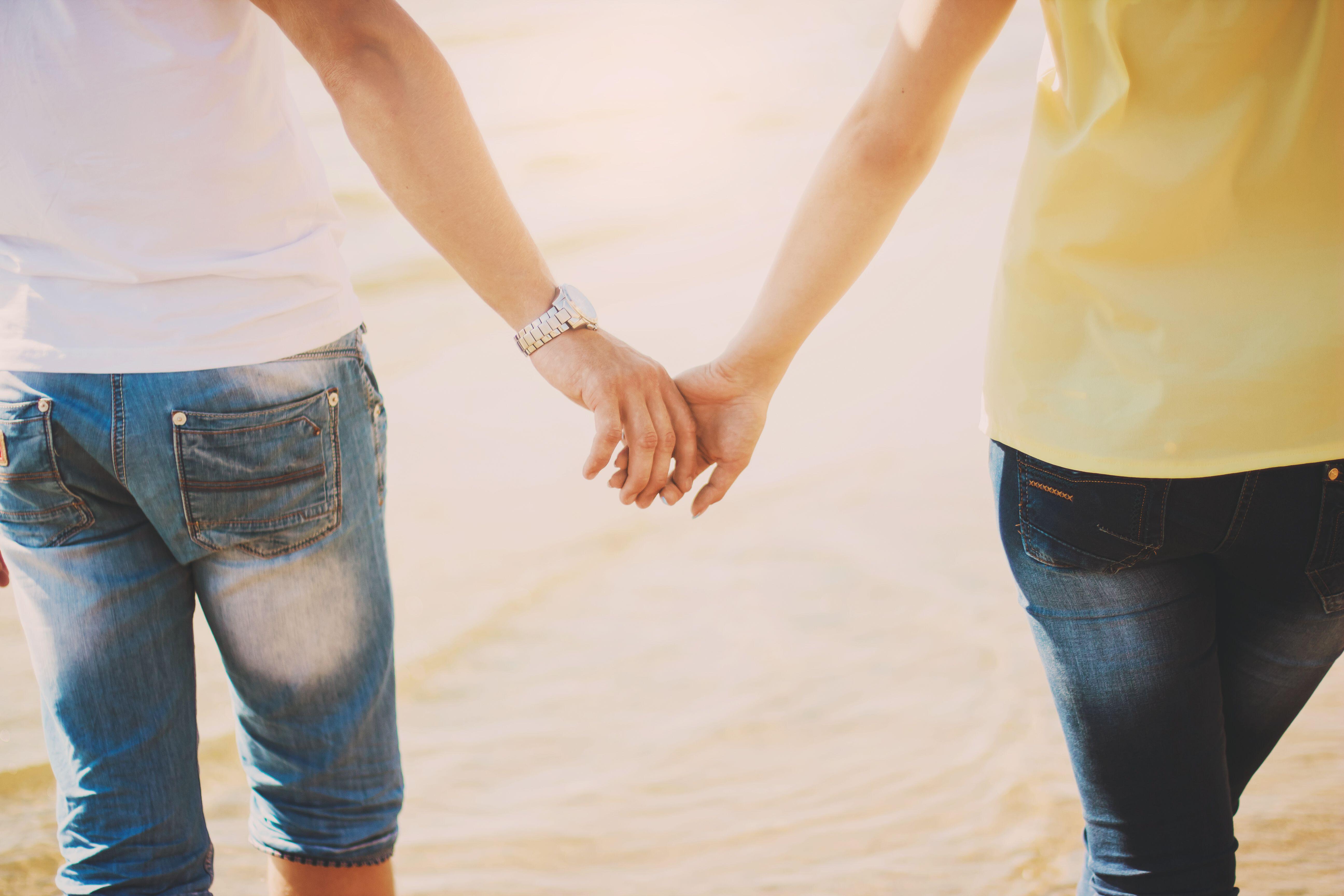 Couples holding hands. Summer in love. Close up of loving couple holding hands on a beach near the sea