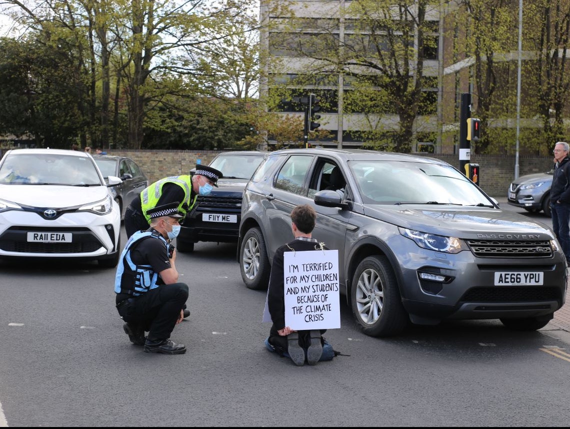 Police speak to a protester kneeling in a road in Cambridge