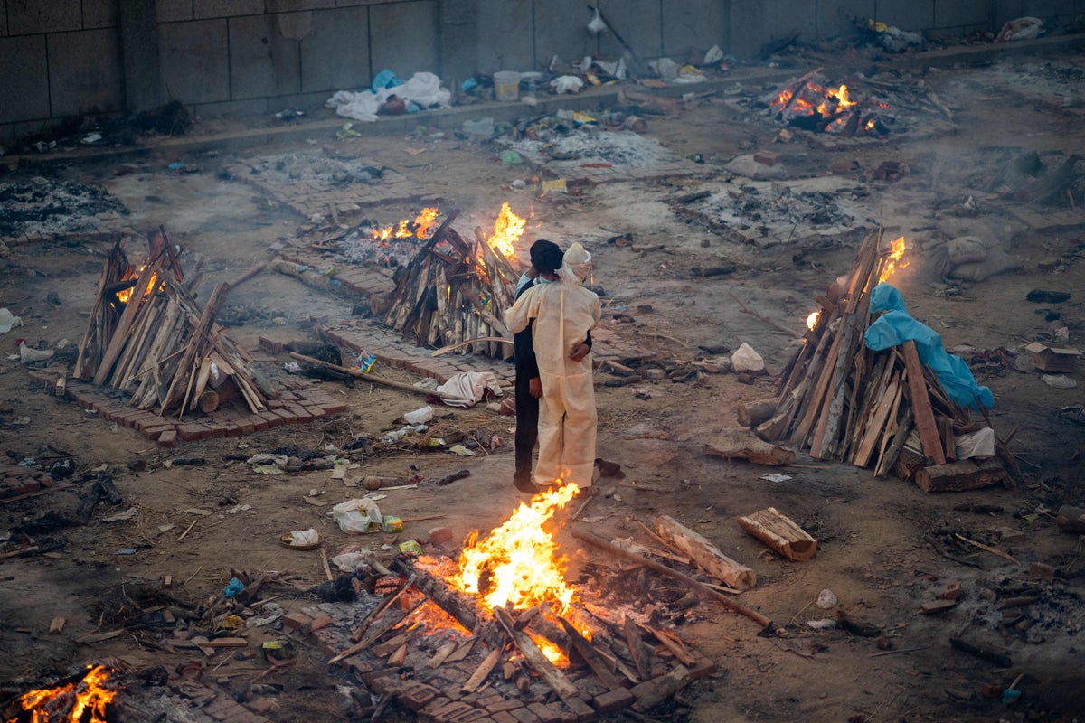 Family members embrace each other amid burning pyres of victims at a cremation ground in New Delhi