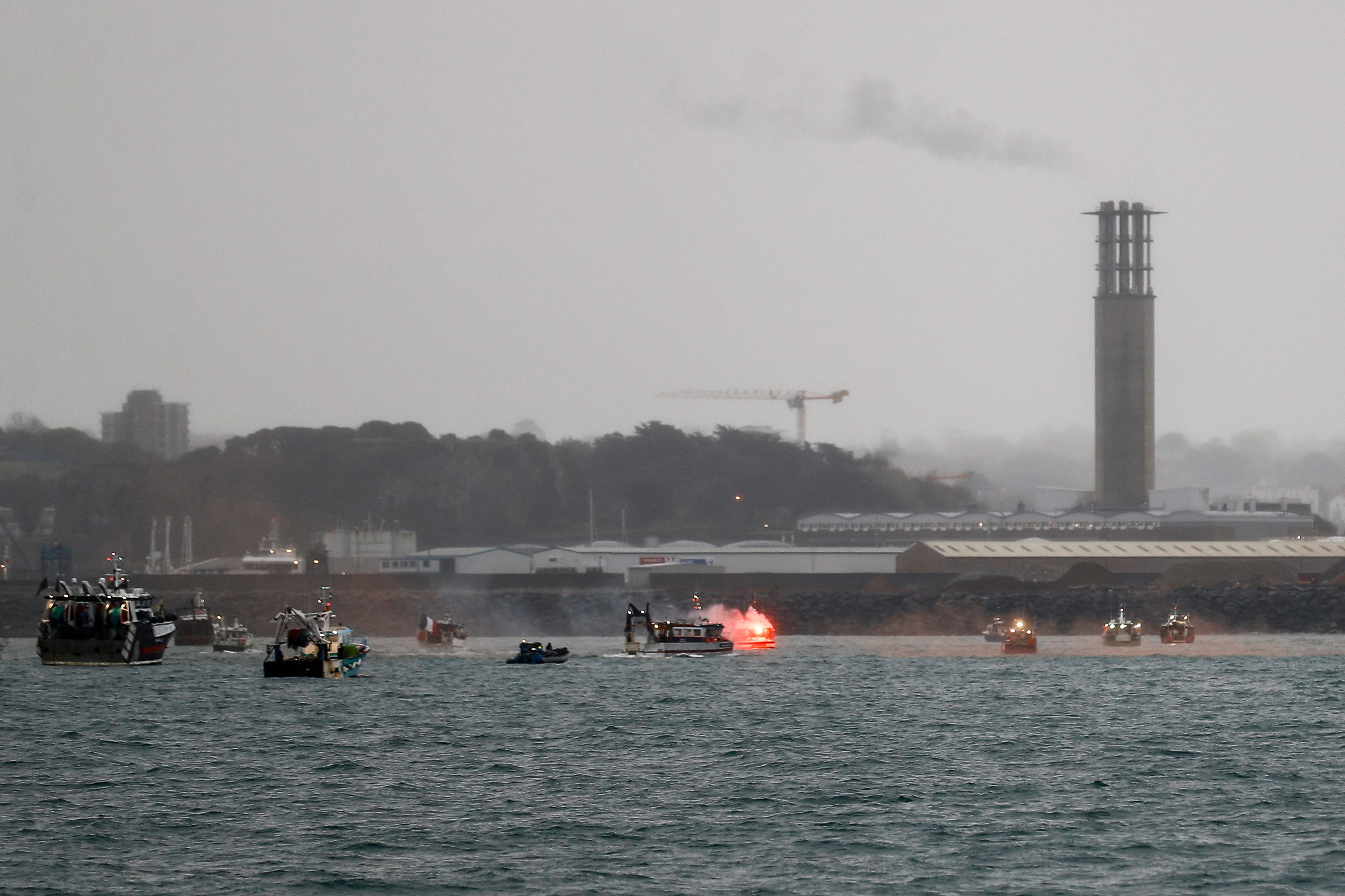 A flare is lit as French fishing boats protest in front of the port of Saint Helier