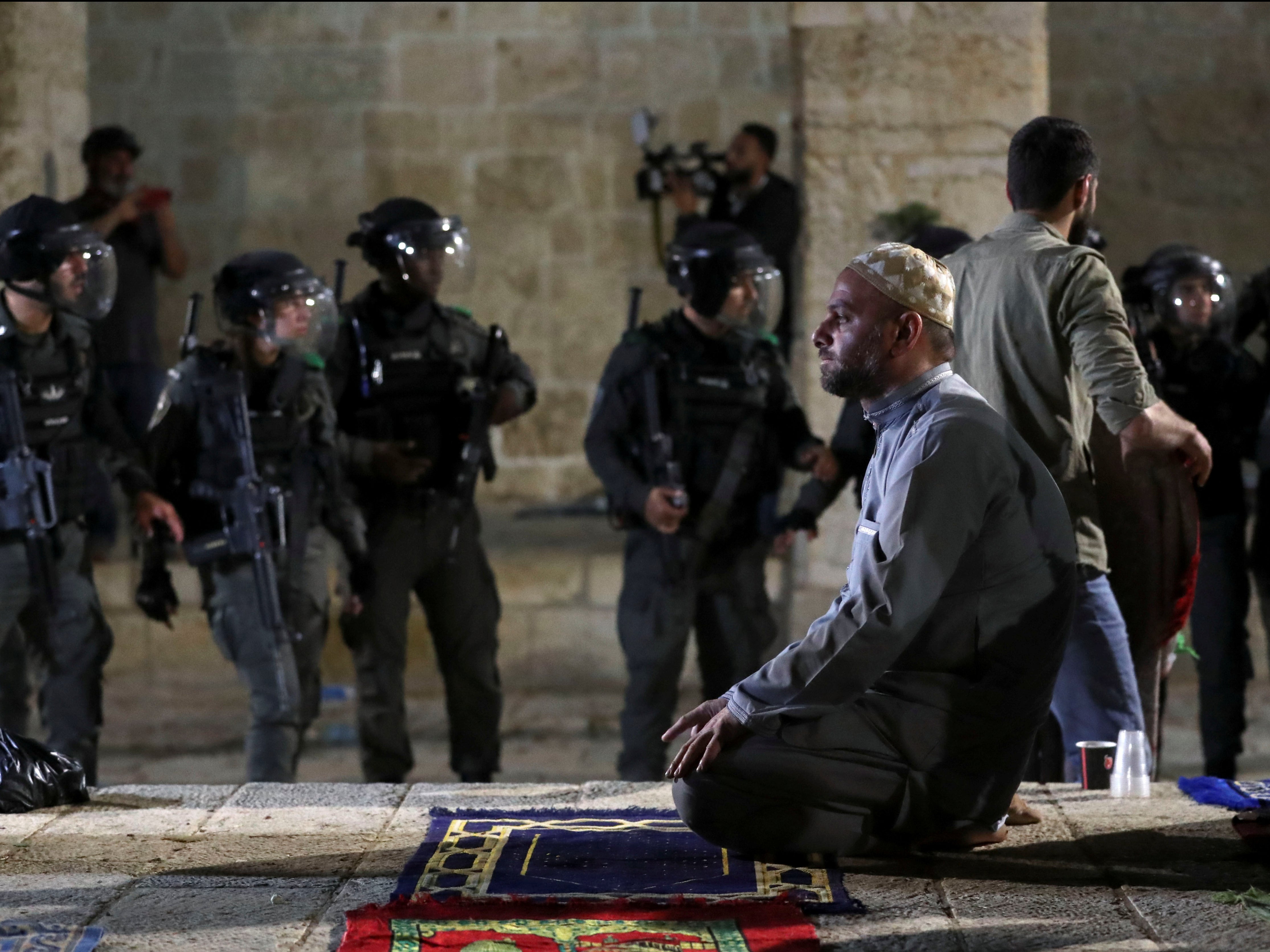 A Palestinian man prays as Israeli police gather during clashes at the compound that houses Al-Aqsa Mosque