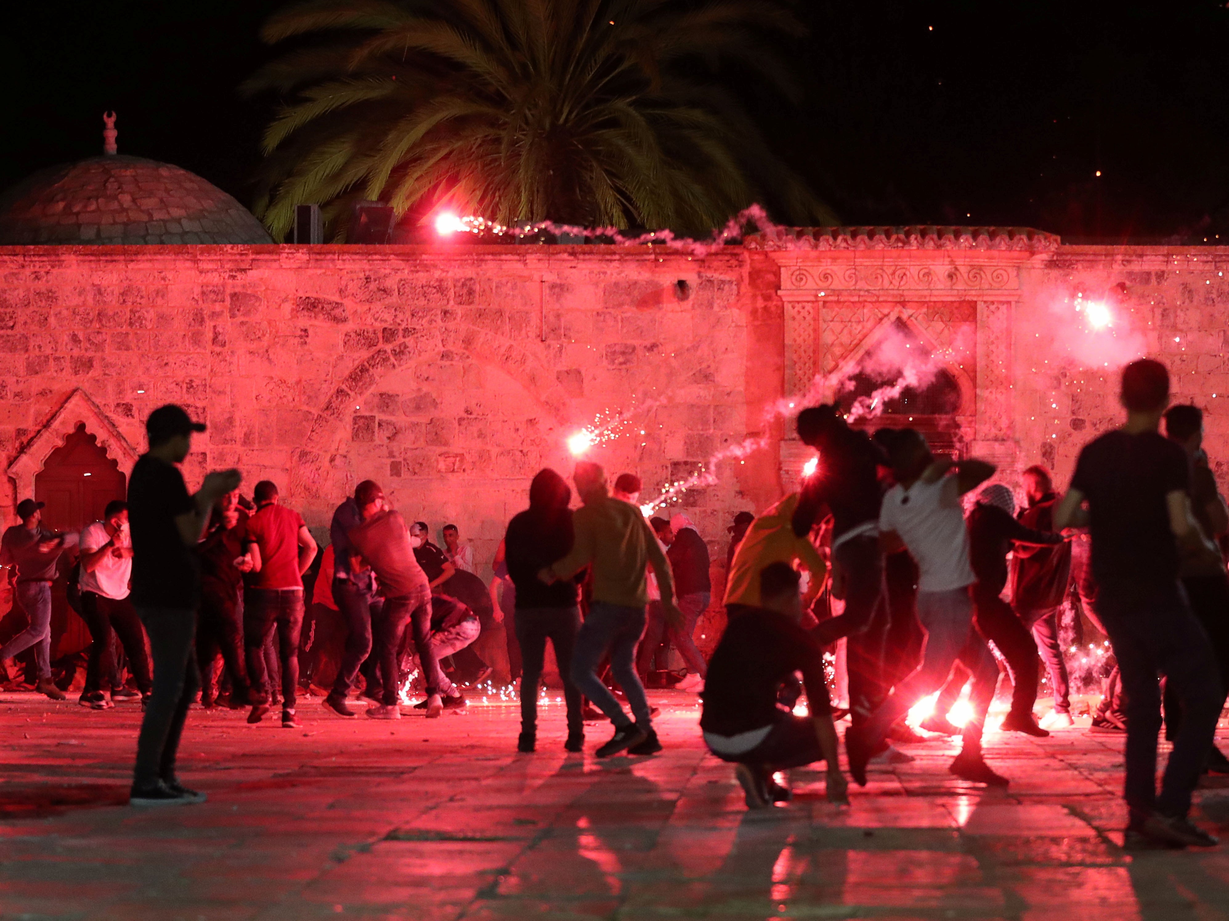 Palestinians react as Israeli police fire stun grenades during clashes at the compound that houses Al-Aqsa Mosque