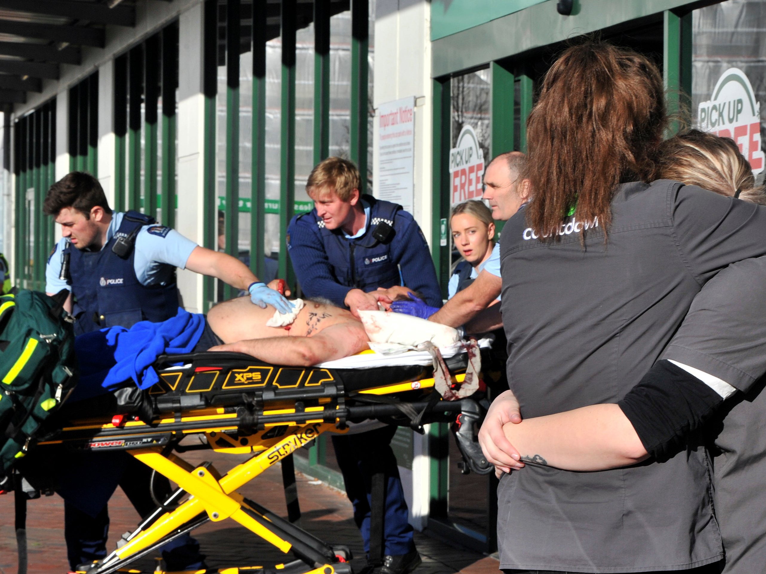 A victim of the supermarket stabbing is taken to hospital as store staff embrace outside