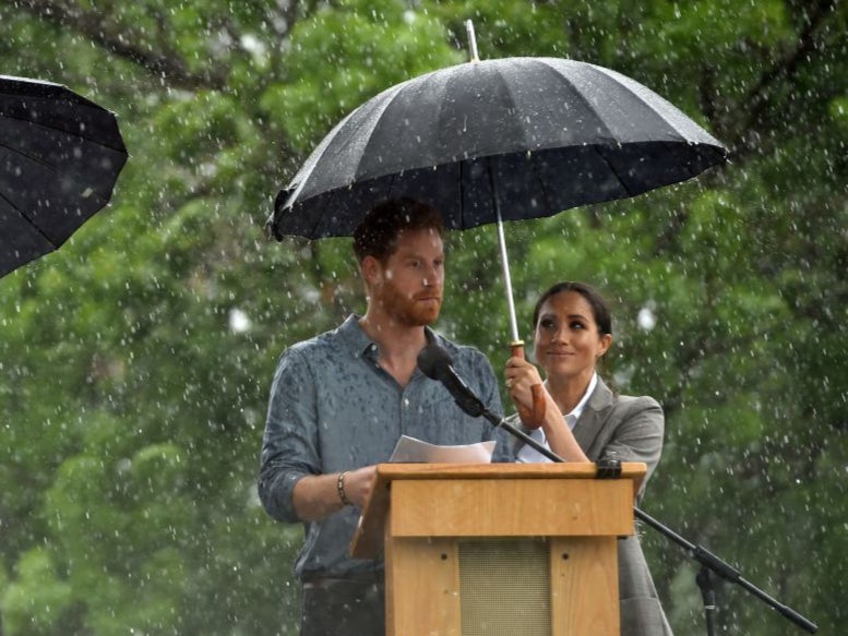 Britain’s Prince Harry speaks to the community as his wife Meghan, Duchess of Sussex holds an umbrella under heavy rain in Australia’s outback town of Dubbo in October 2018