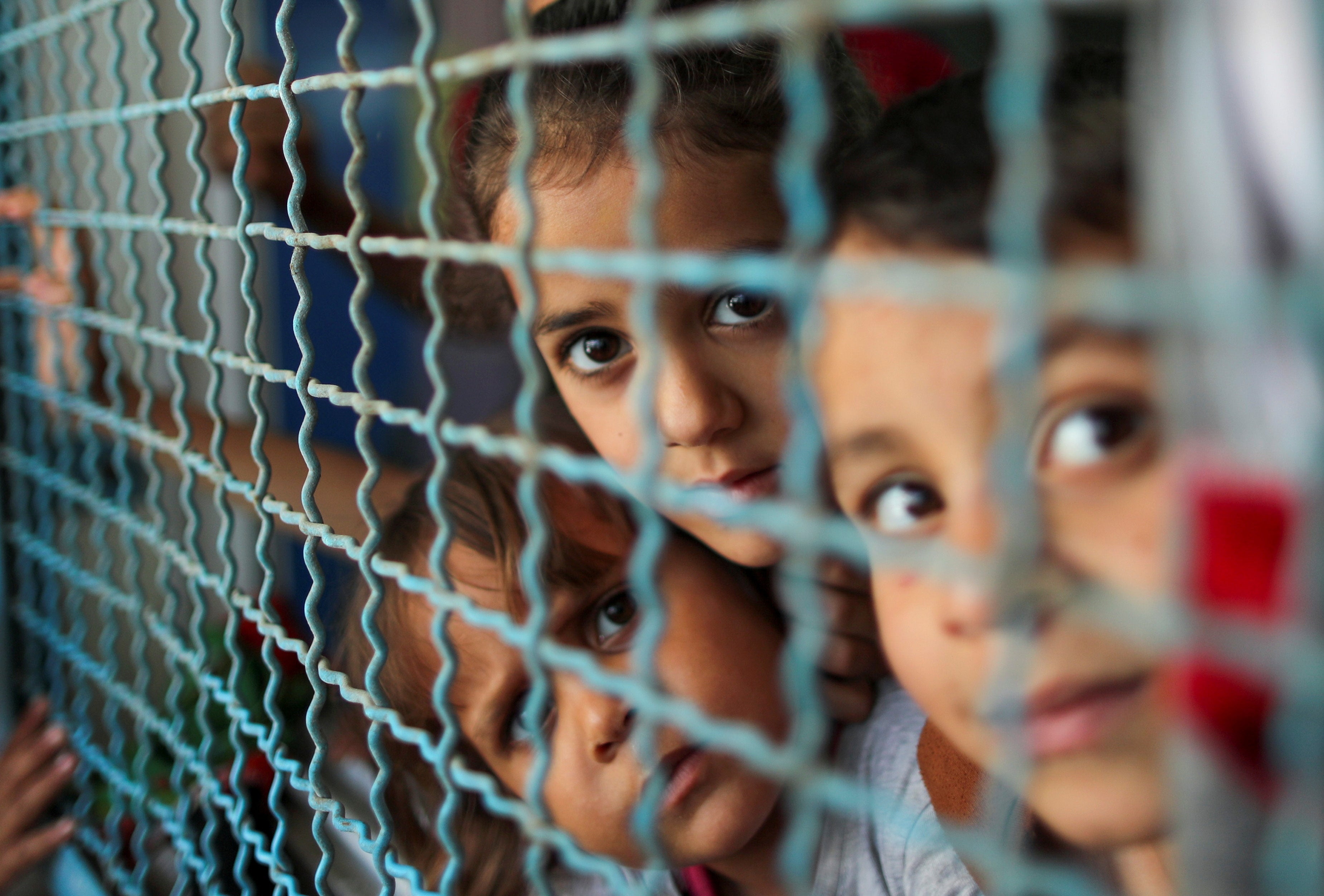 Palestinian children, who fled their homes due to Israeli air and artillery strikes, look through a window fence at a United Nations-run school where they take refuge, in Gaza City