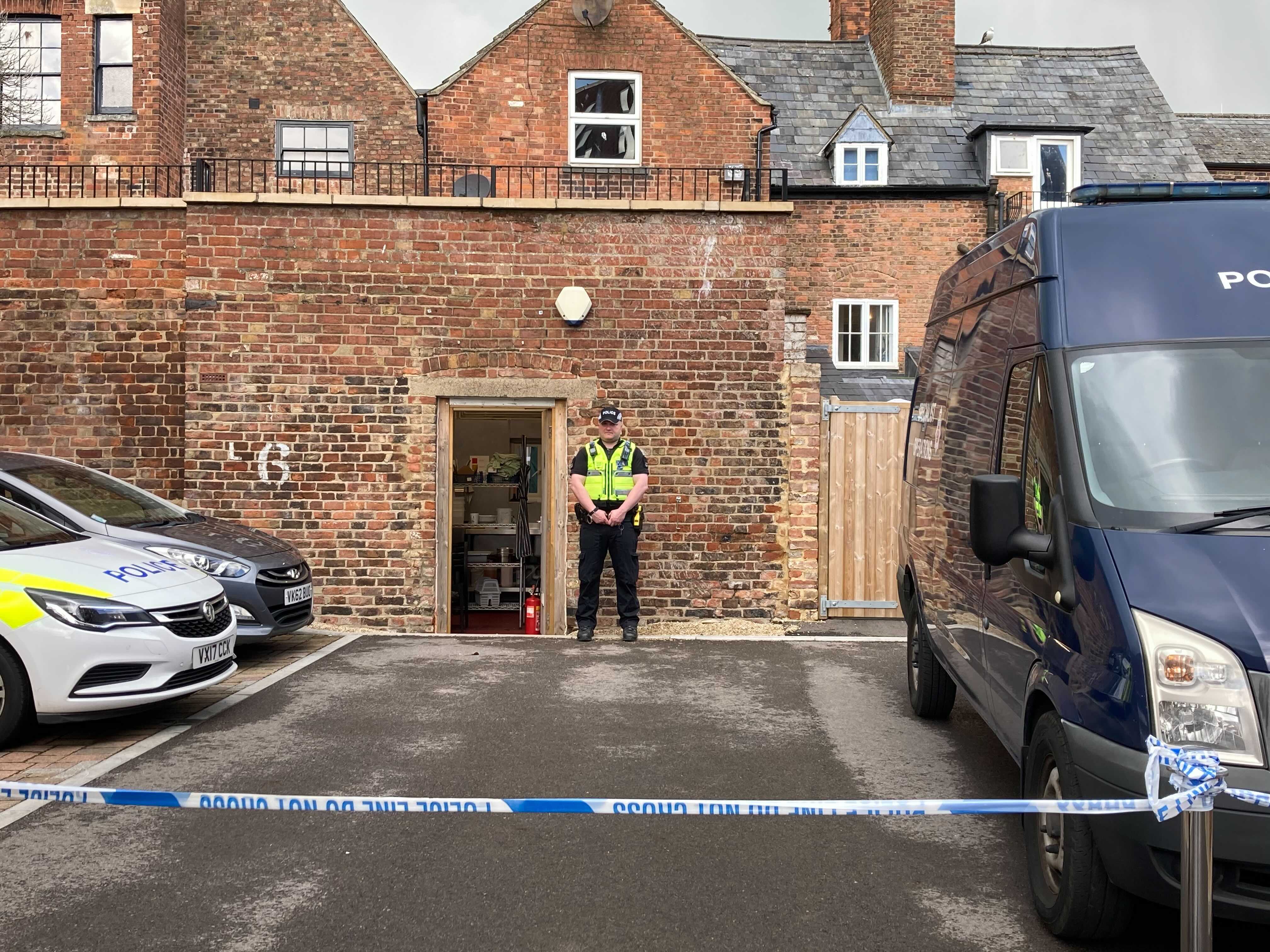 A police officer stands on duty at the rear entrance of the cafe