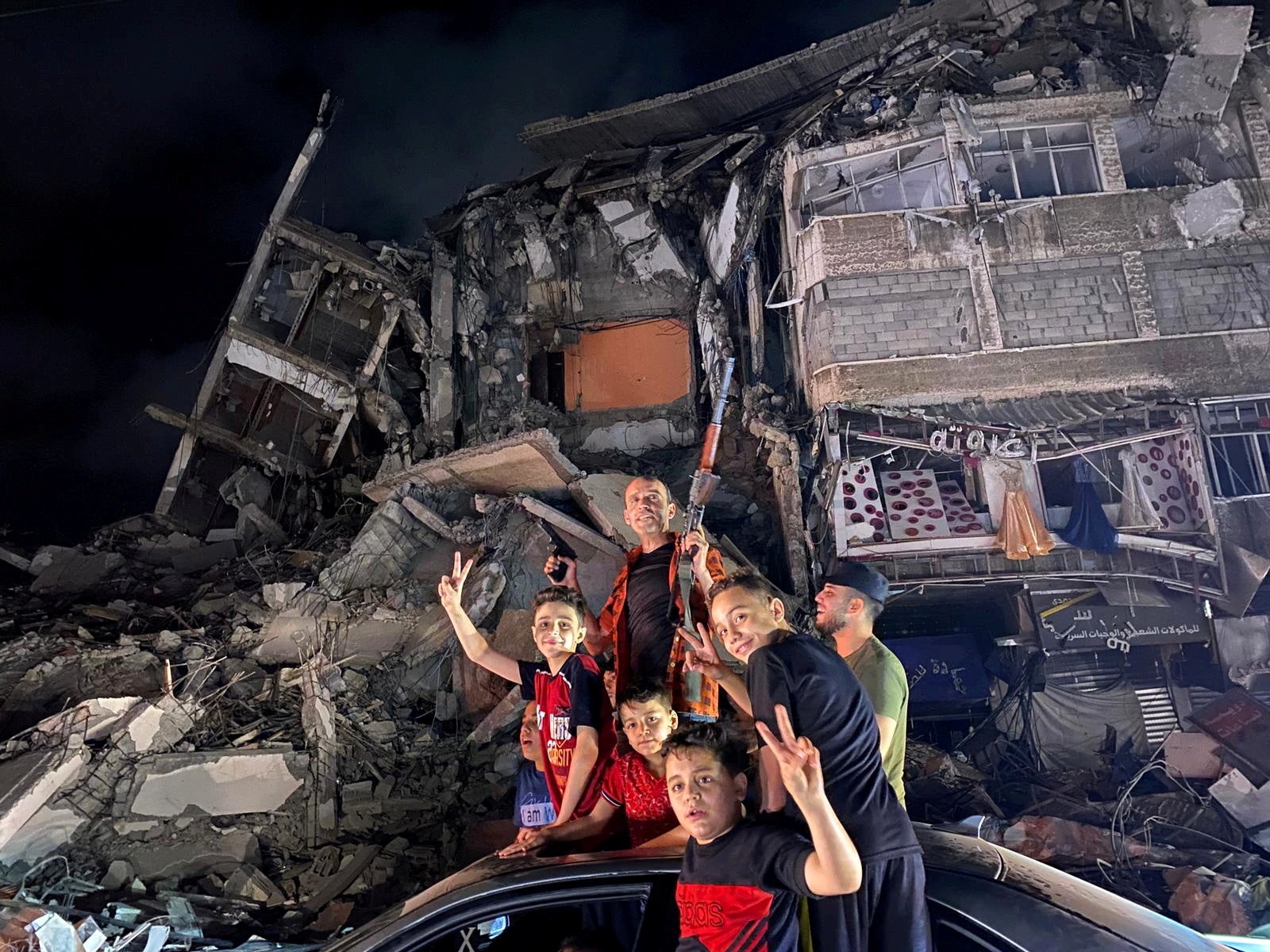 People gesture near the rubble of a damaged building as Palestinians celebrate in the streets following a ceasefire in Gaza