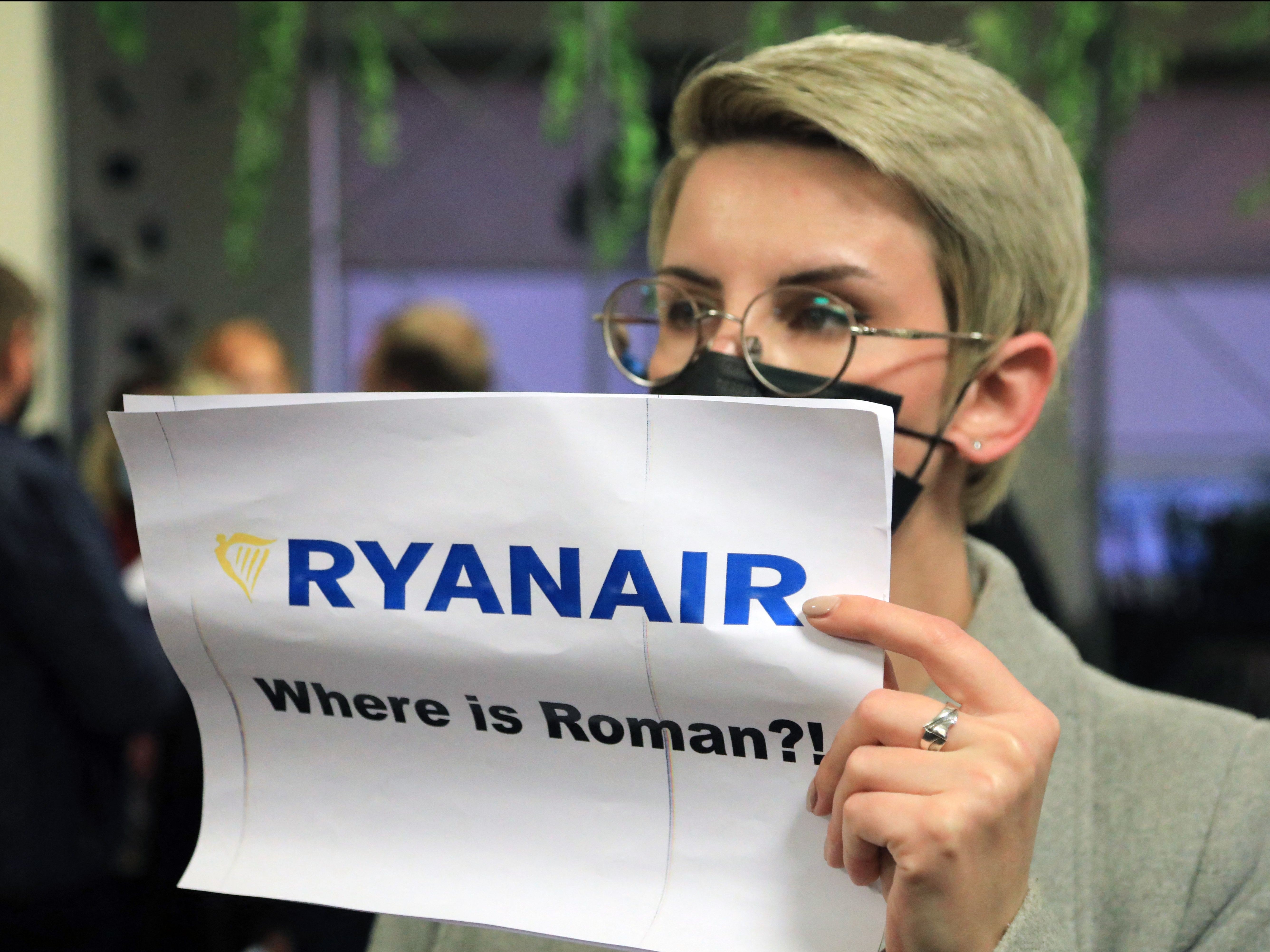 A woman with poster reading ‘Where is Roman [Protasevich]?!’ as passengers disembark from Ryanair plane in Athens