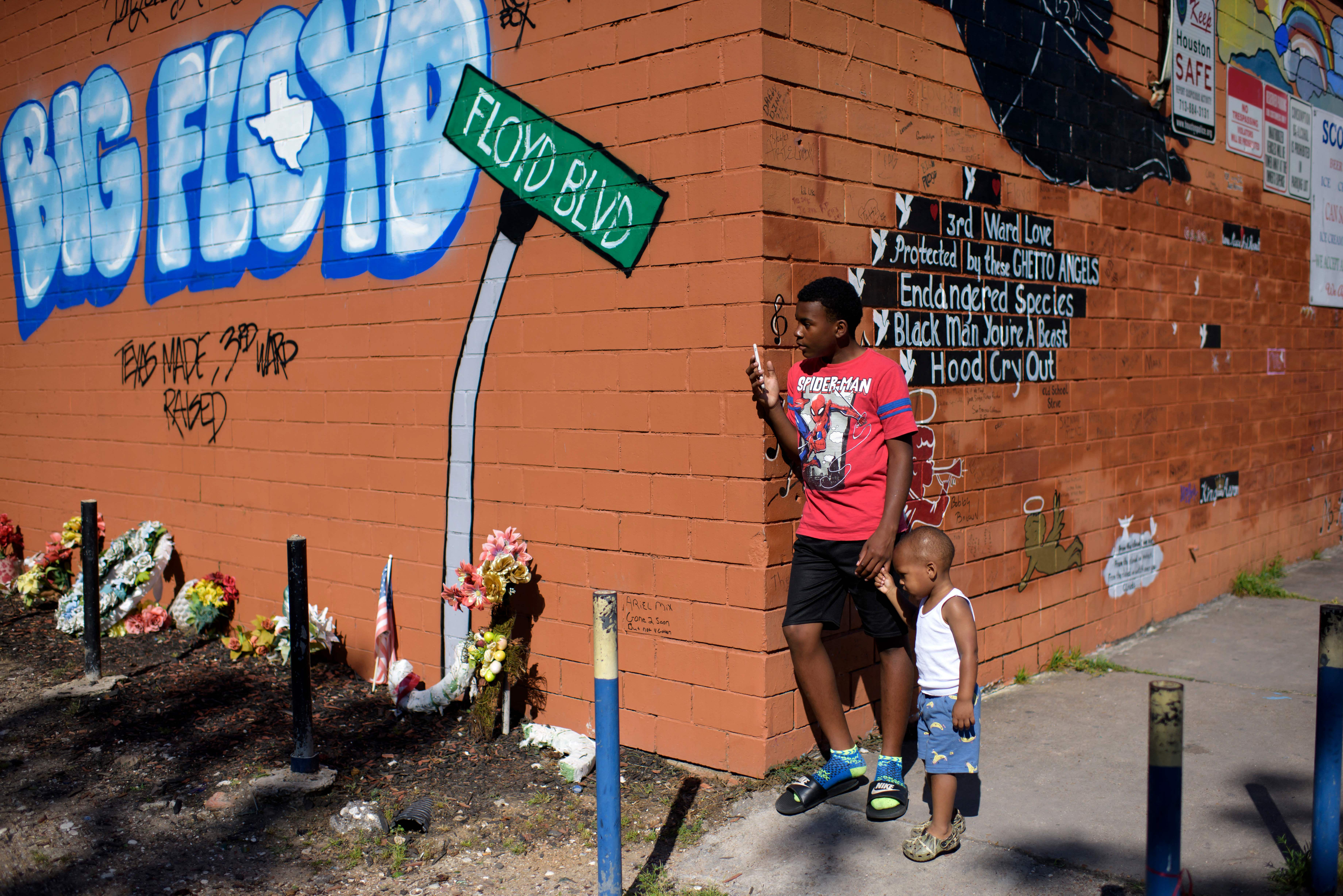 A boy and his younger brother stand next to a mural of George Floyd at the corner of Scotts Food Mart in the third ward in Houston, Texas, April 20, 2021. - Sacked police officer Derek Chauvin was convicted of murder and manslaughter on april 20 in the death of African-American George Floyd in a case that roiled the United States for almost a year, laying bare deep racial divisions.