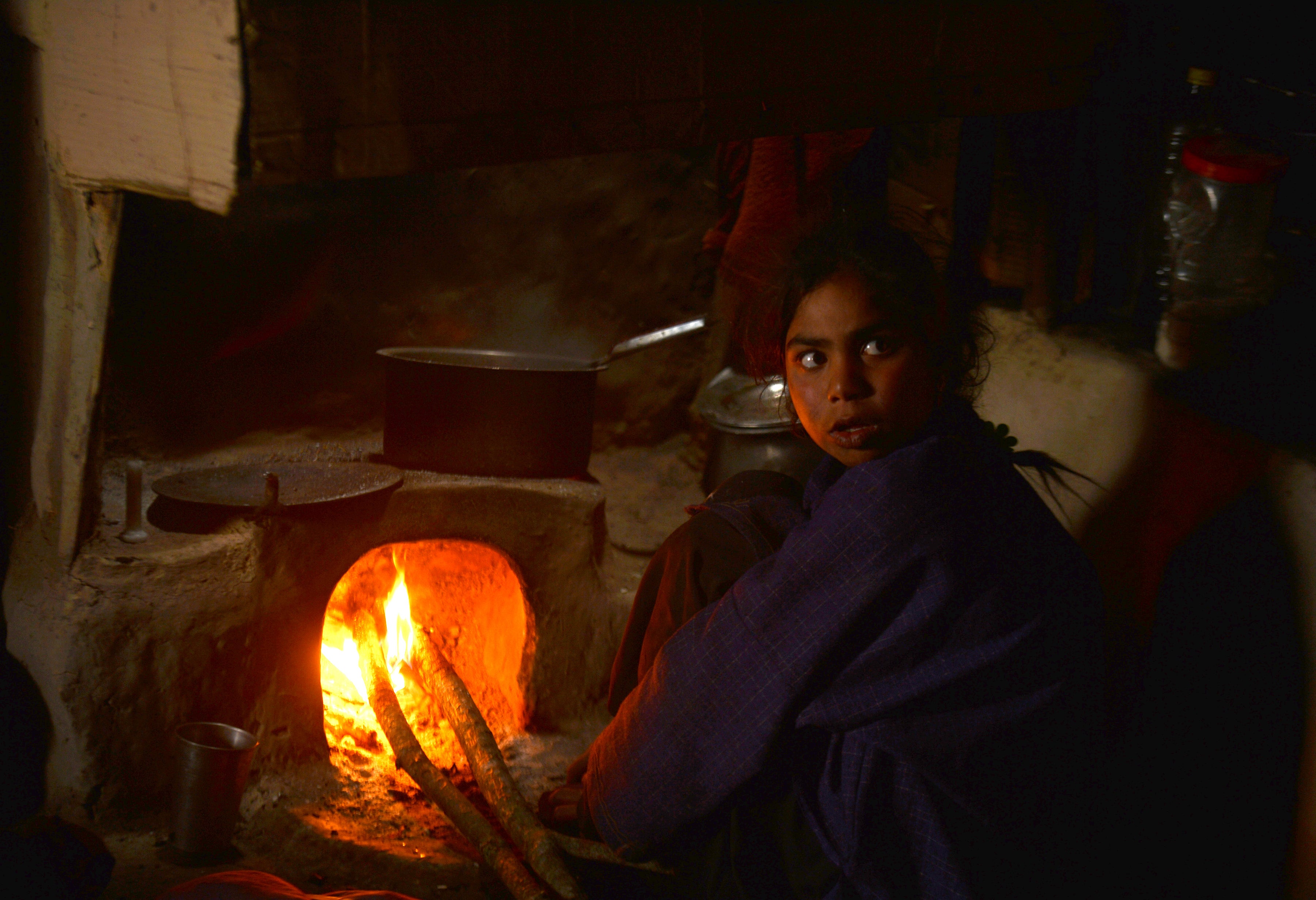 A Kashmiri girl warms herself next to a traditional oven inside a mud house on the outskirts of Srinagar