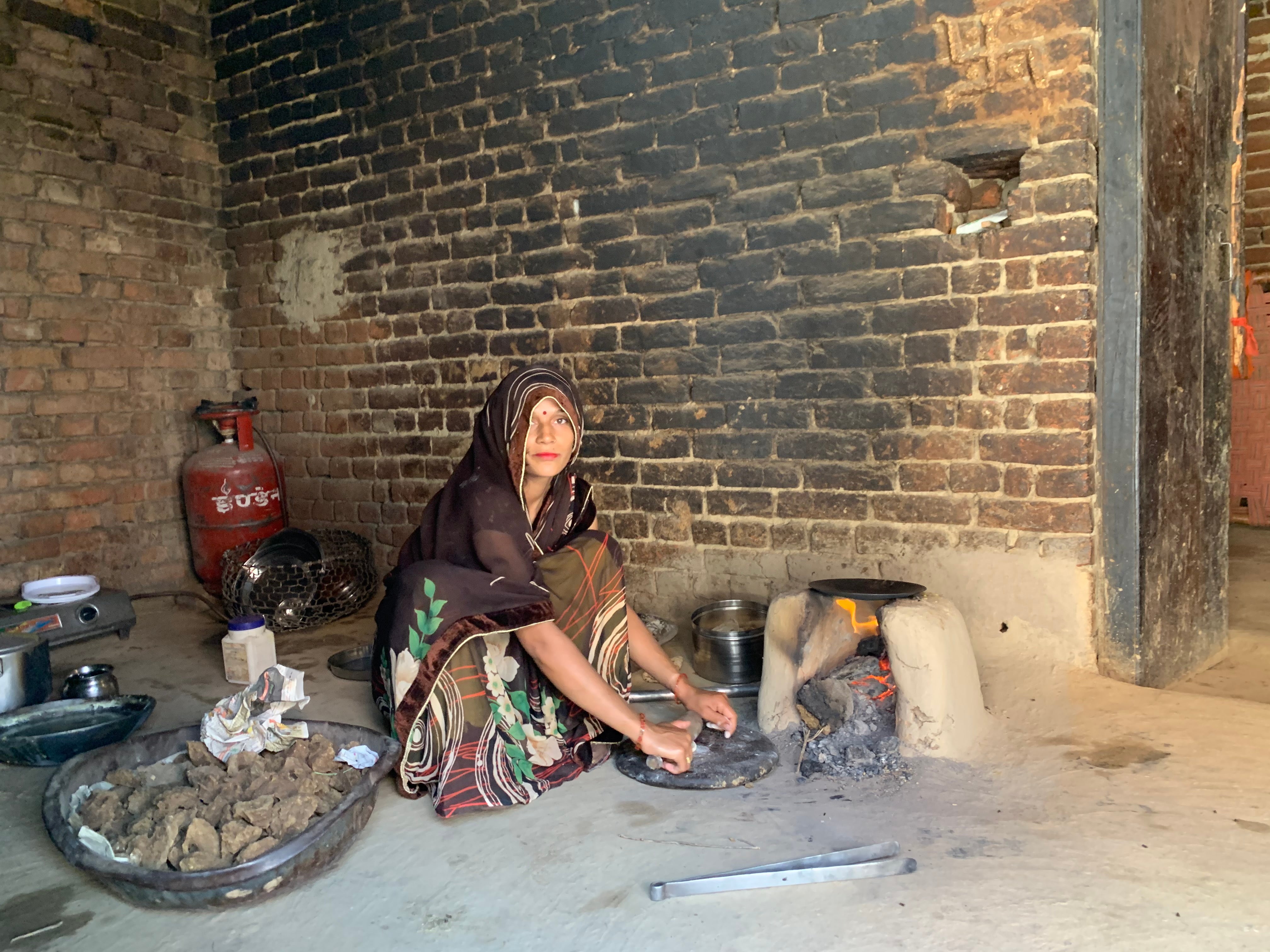 Disha Sharma cooks on the mud stove while a functional gas cylinder and gas stove sits in the corner