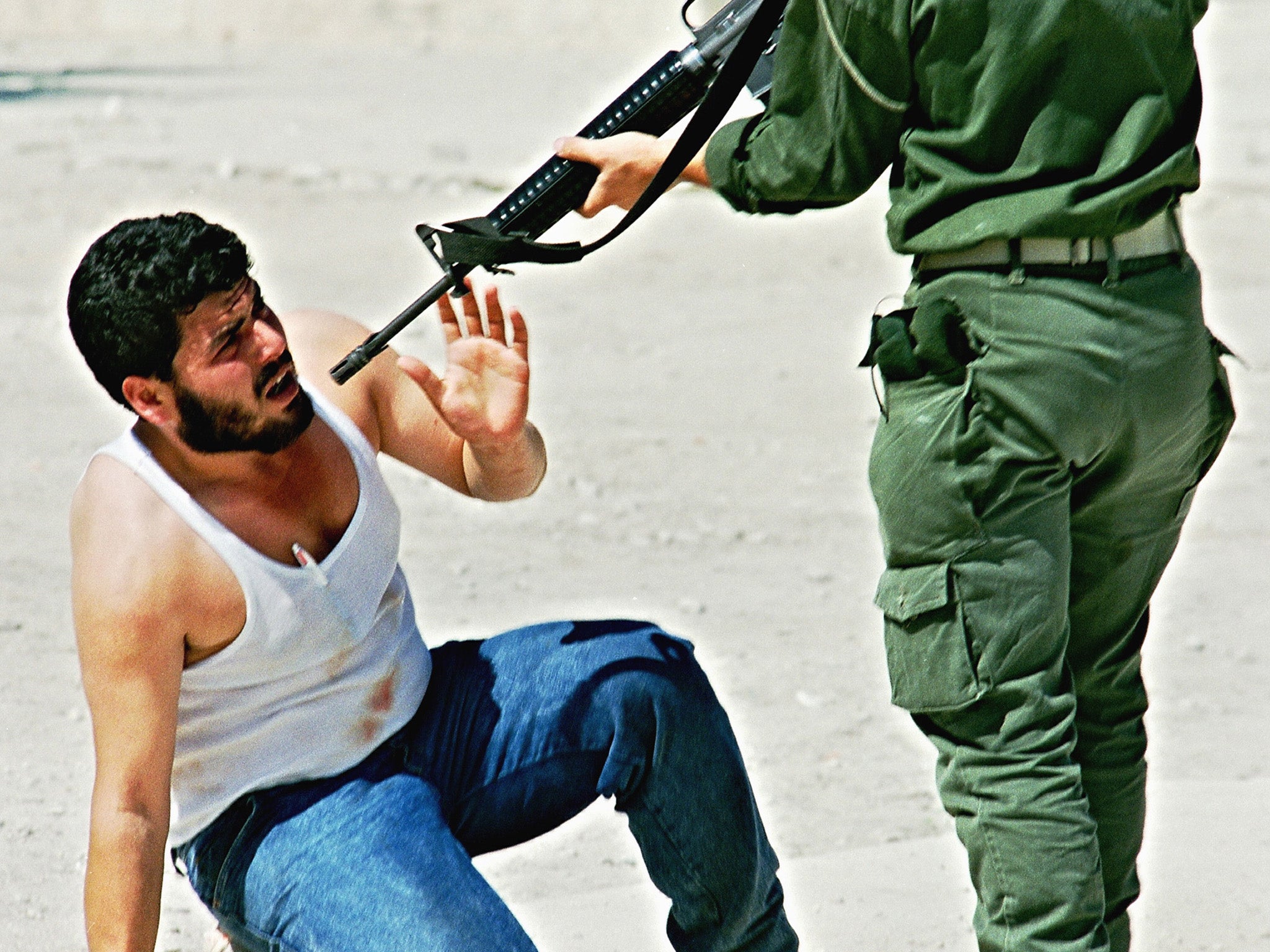 An Israeli border officer points his rifle at a Palestinian man in October 1990