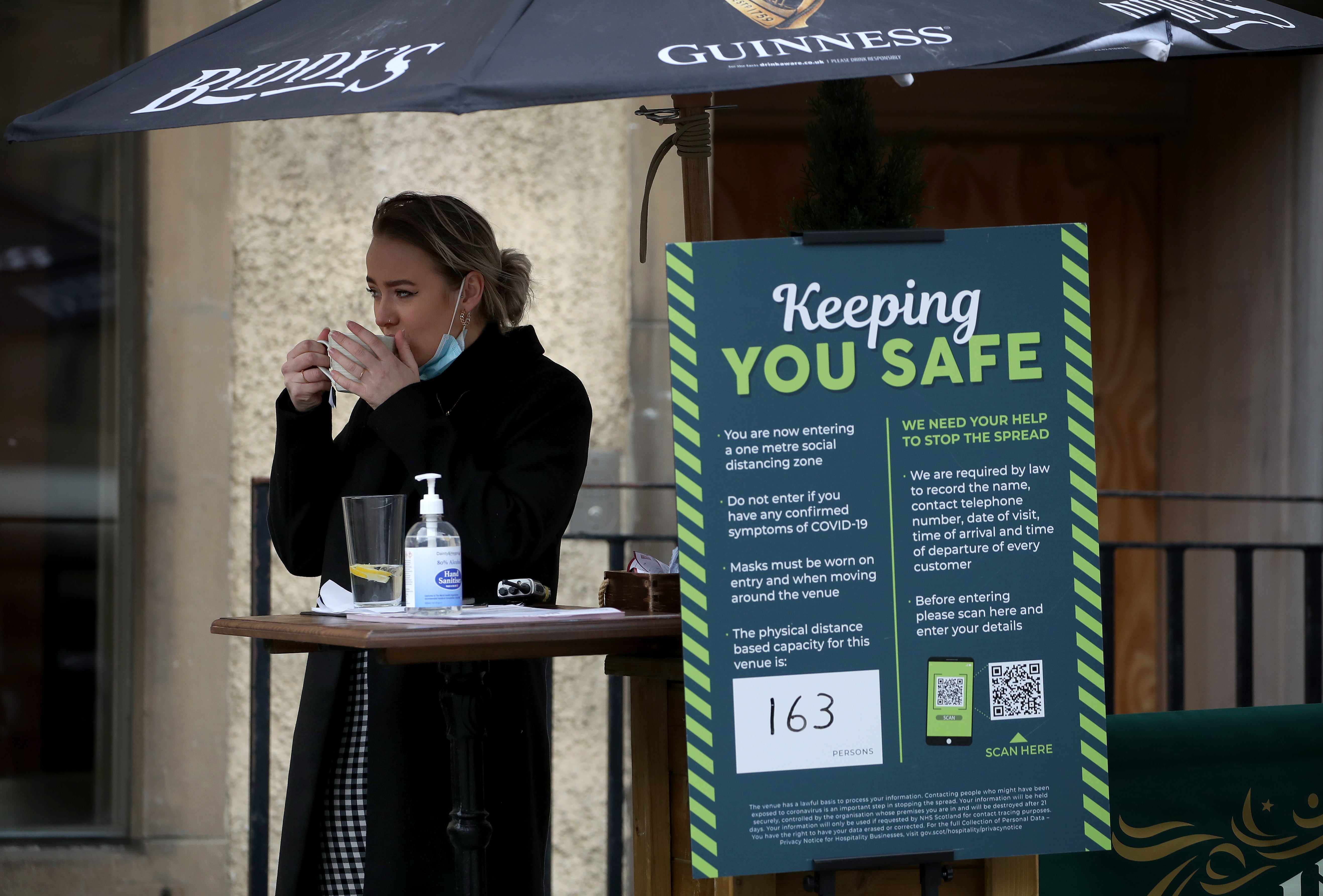 A woman drinks from a mug outside a hospitality venue