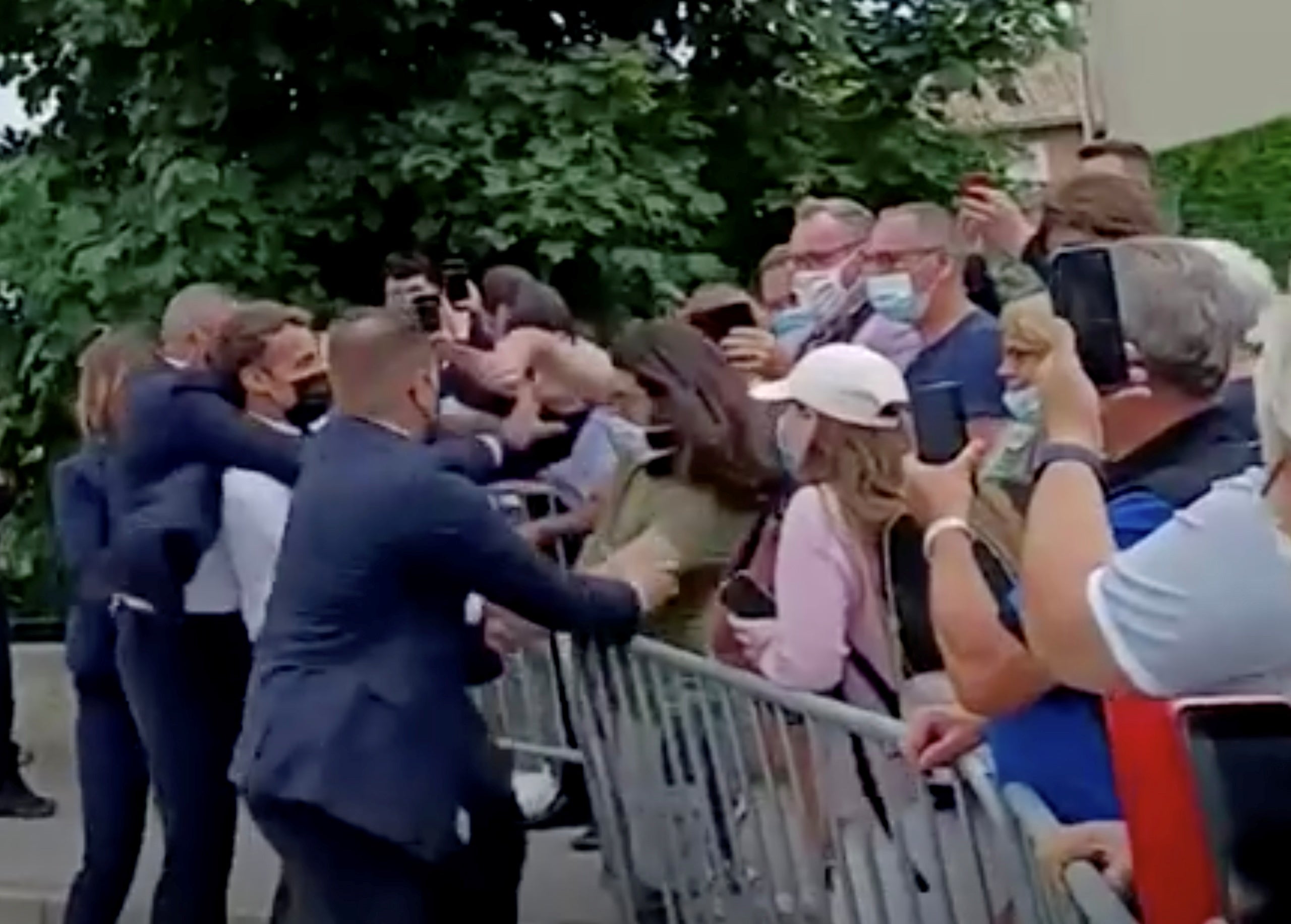 French President Emmanuel Macron is protected by a security member after getting slapped