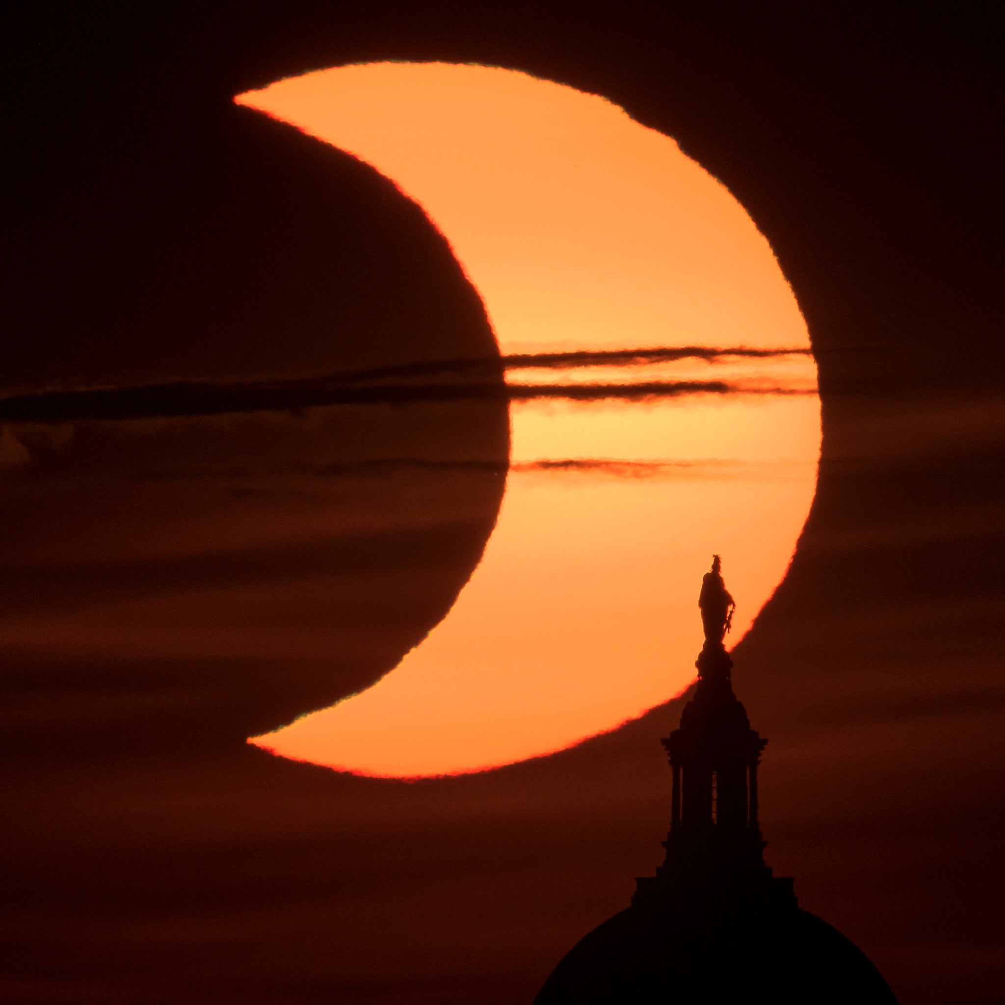 The sun rises behind the Statue of Freedom on top of the United States Capitol Building