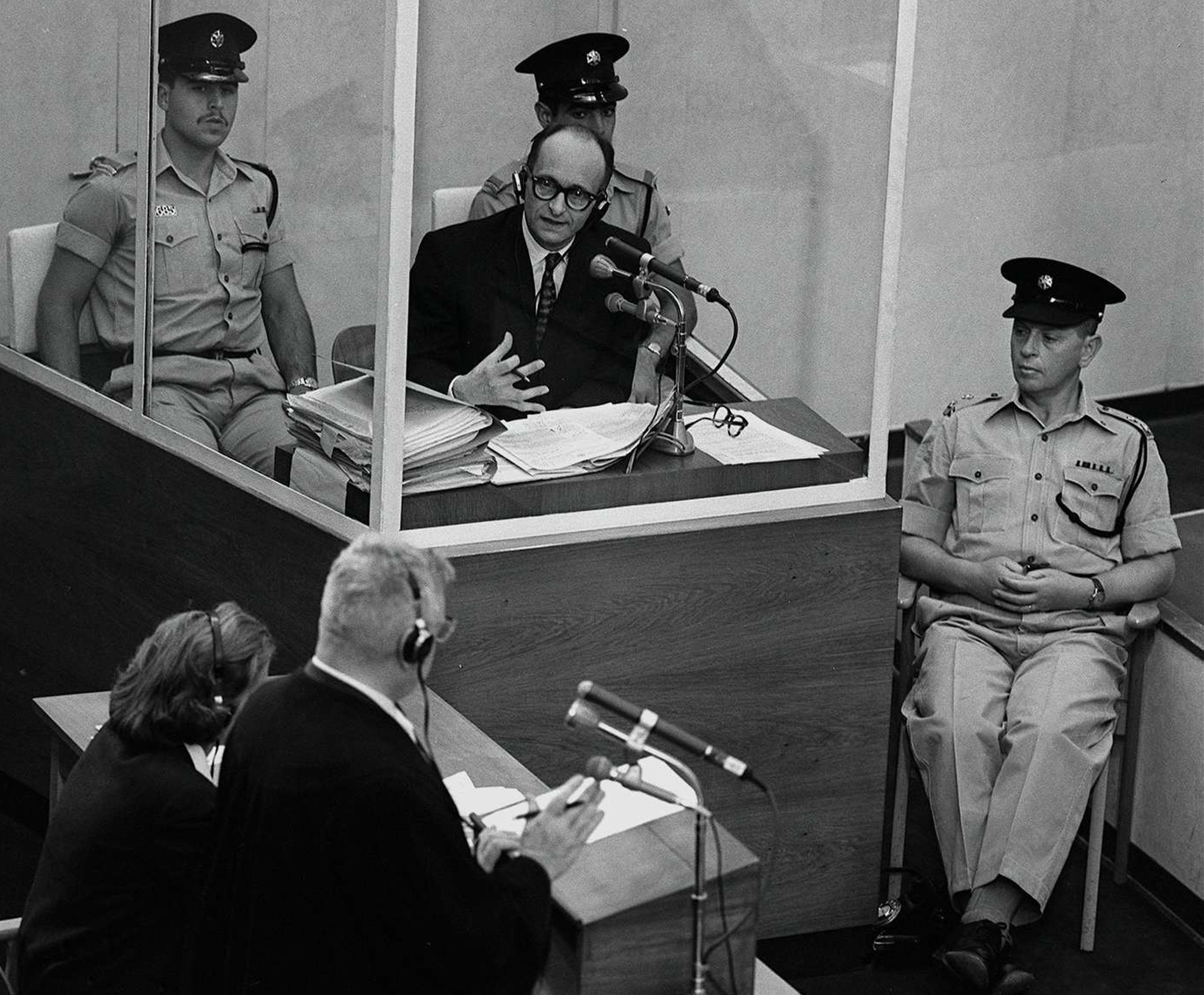 Nazi war criminal Adolph Eichmann stands in a protective glass booth flanked by Israeli police during his trial on 22 June 1961 in Jerusalem