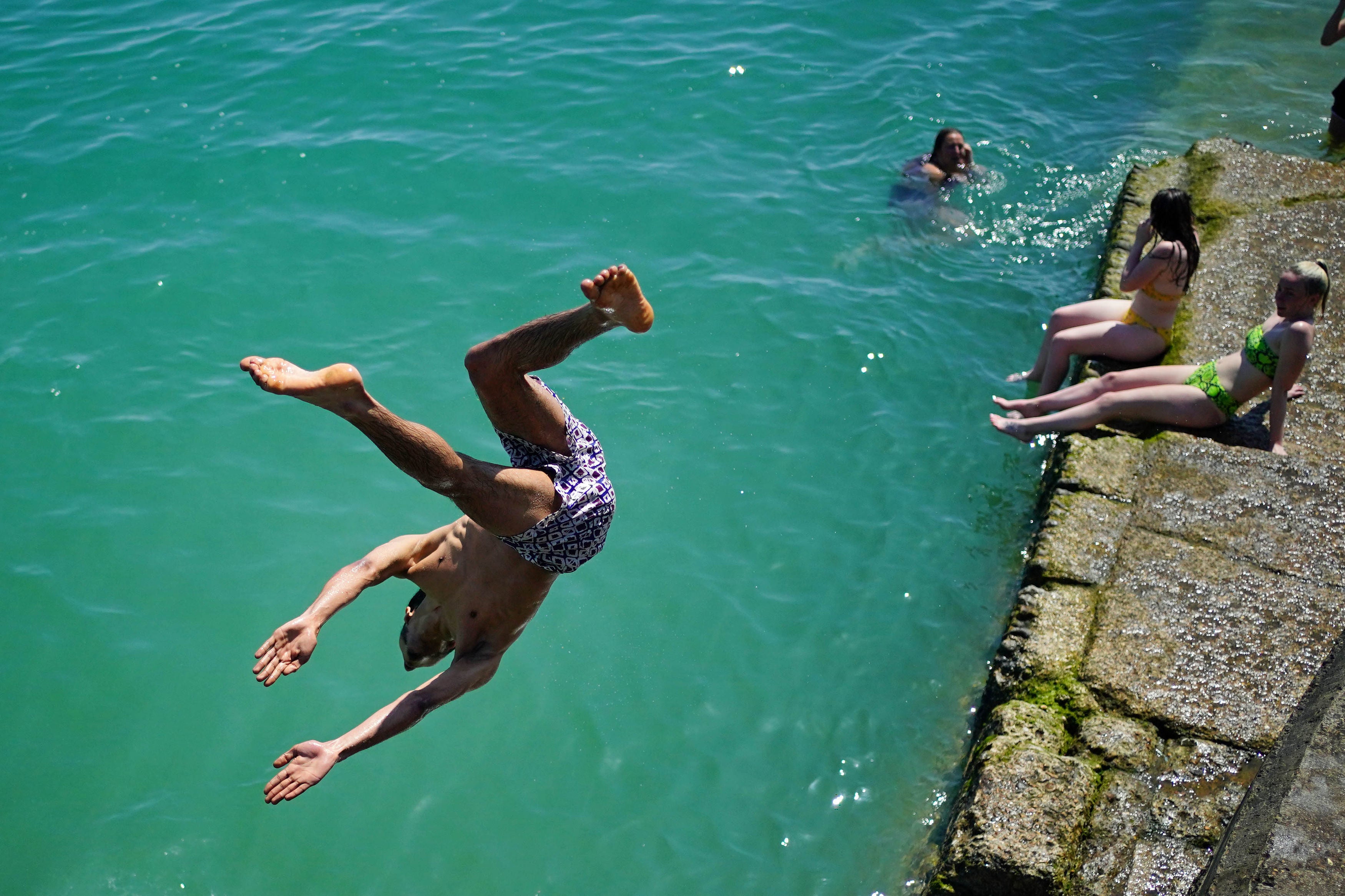 A man dives into the sea whilst people enjoy the sunshine on Brighton beach