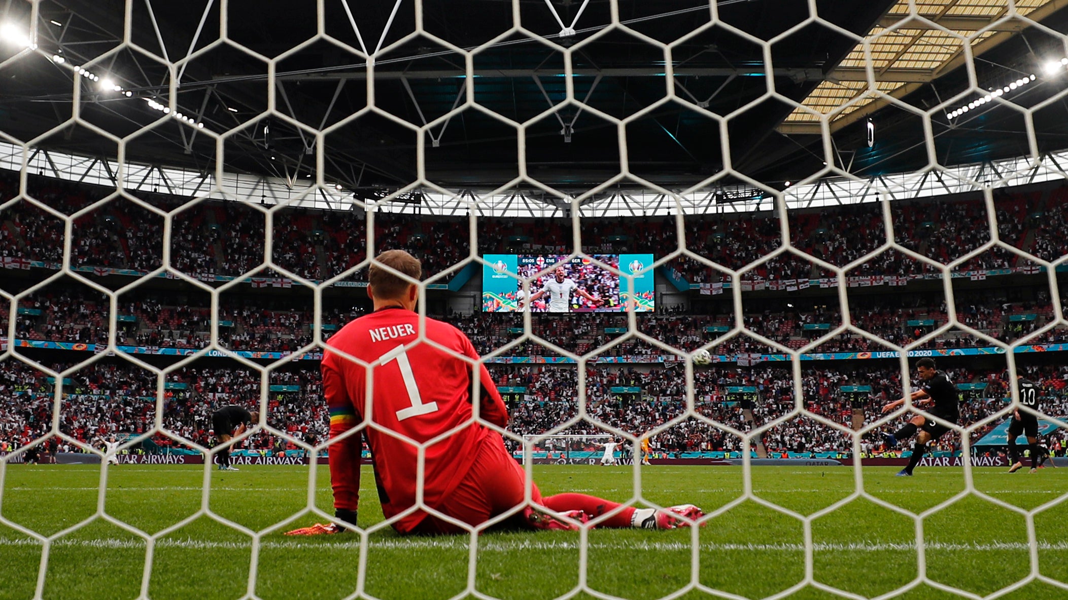 Germany goalkeeper Manuel Neuer sits on the ground while the video screen shows England’s Harry Kane celebrating