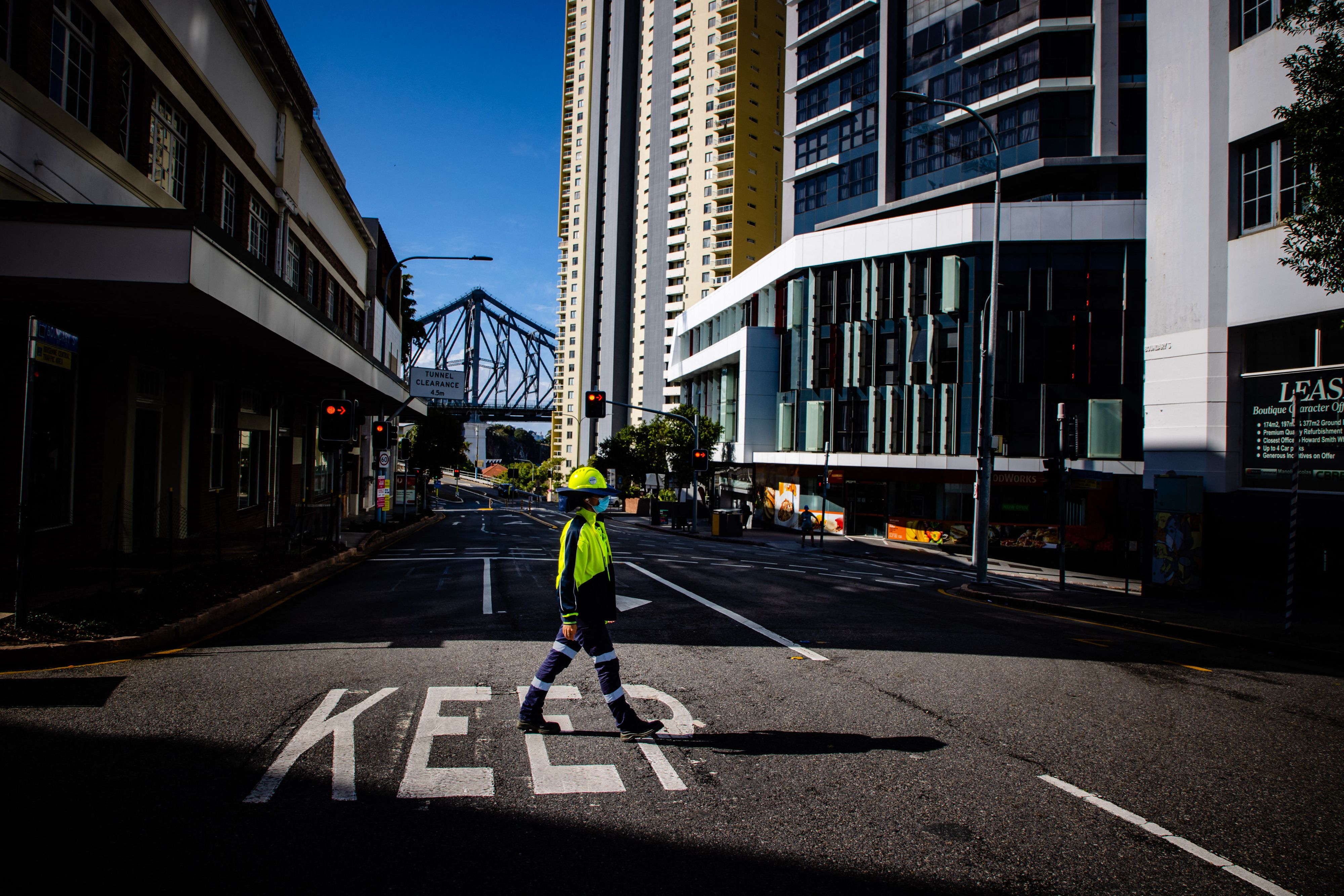 A traffic control worker walks across a deserted street in Brisbane, Australia as lockdown restrictions have been extended by 72 hours for the city