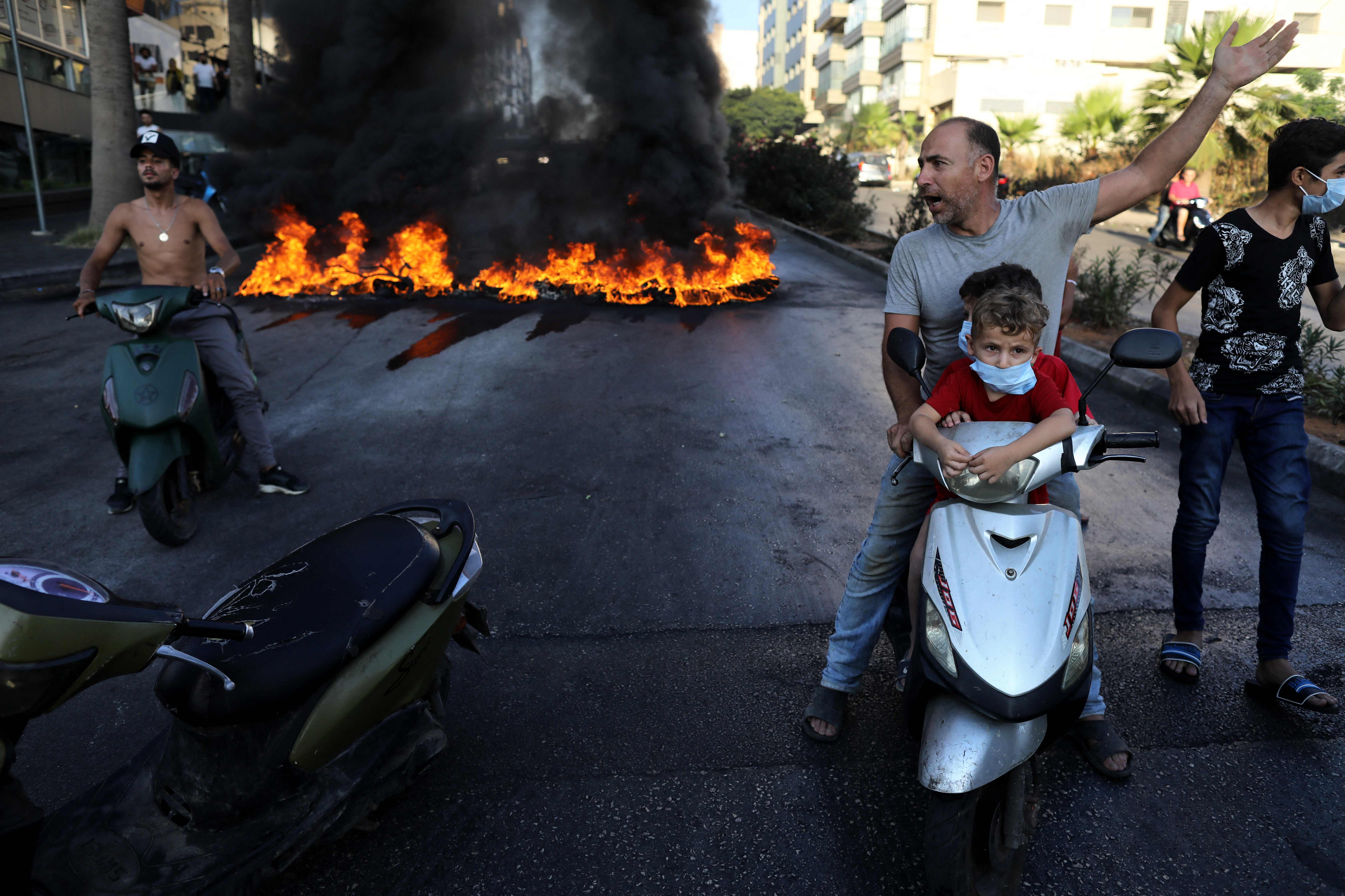 A Lebanese man on a scooter with two children gestures near tires set on fire during a protest at a main road in Lebanon’s capital Beirut against dire conditions amidst the ongoing economical and political crisis