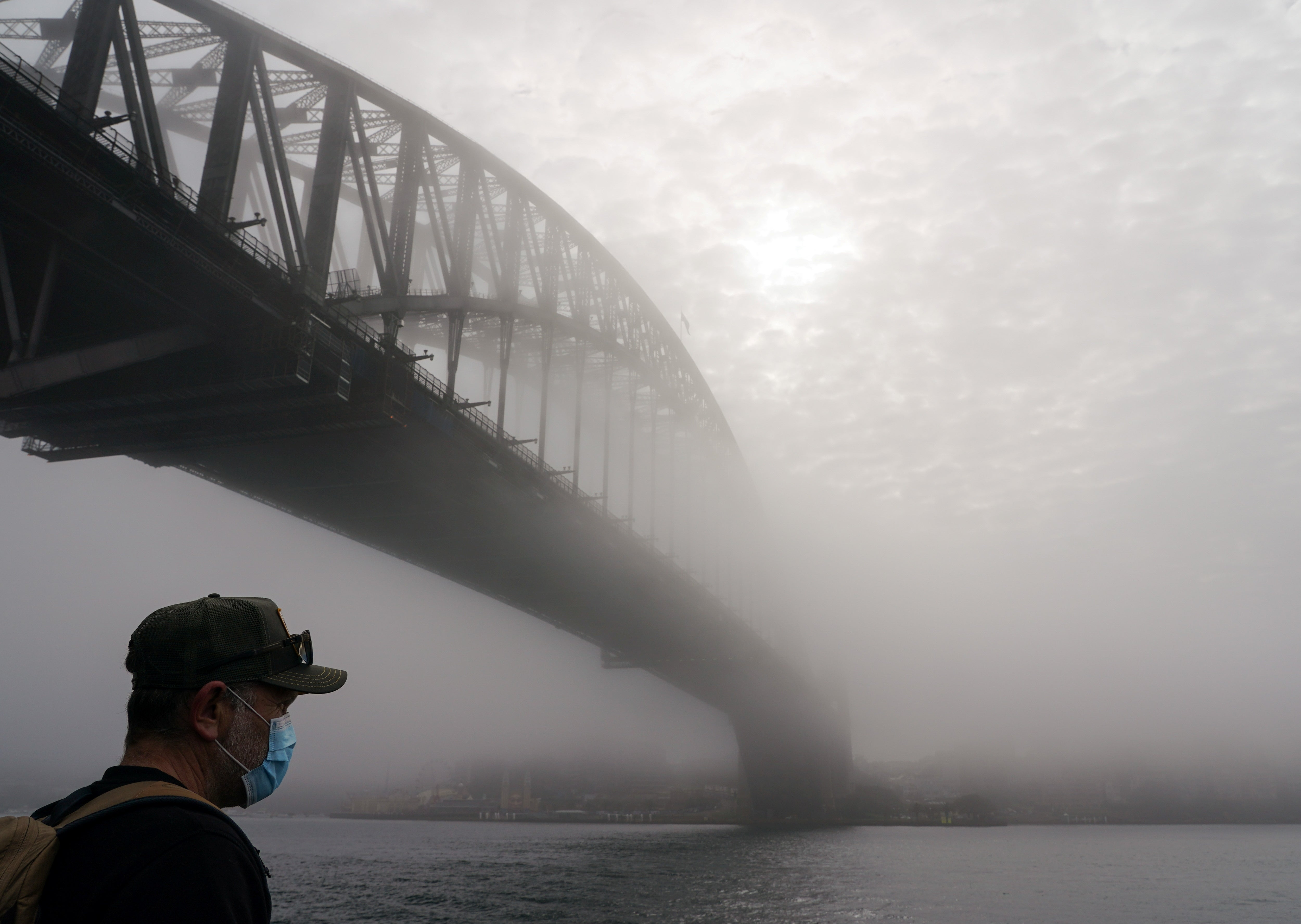 Uncertain outlook. A man wearing a protective face mask next to the Sydney Harbour Bridge