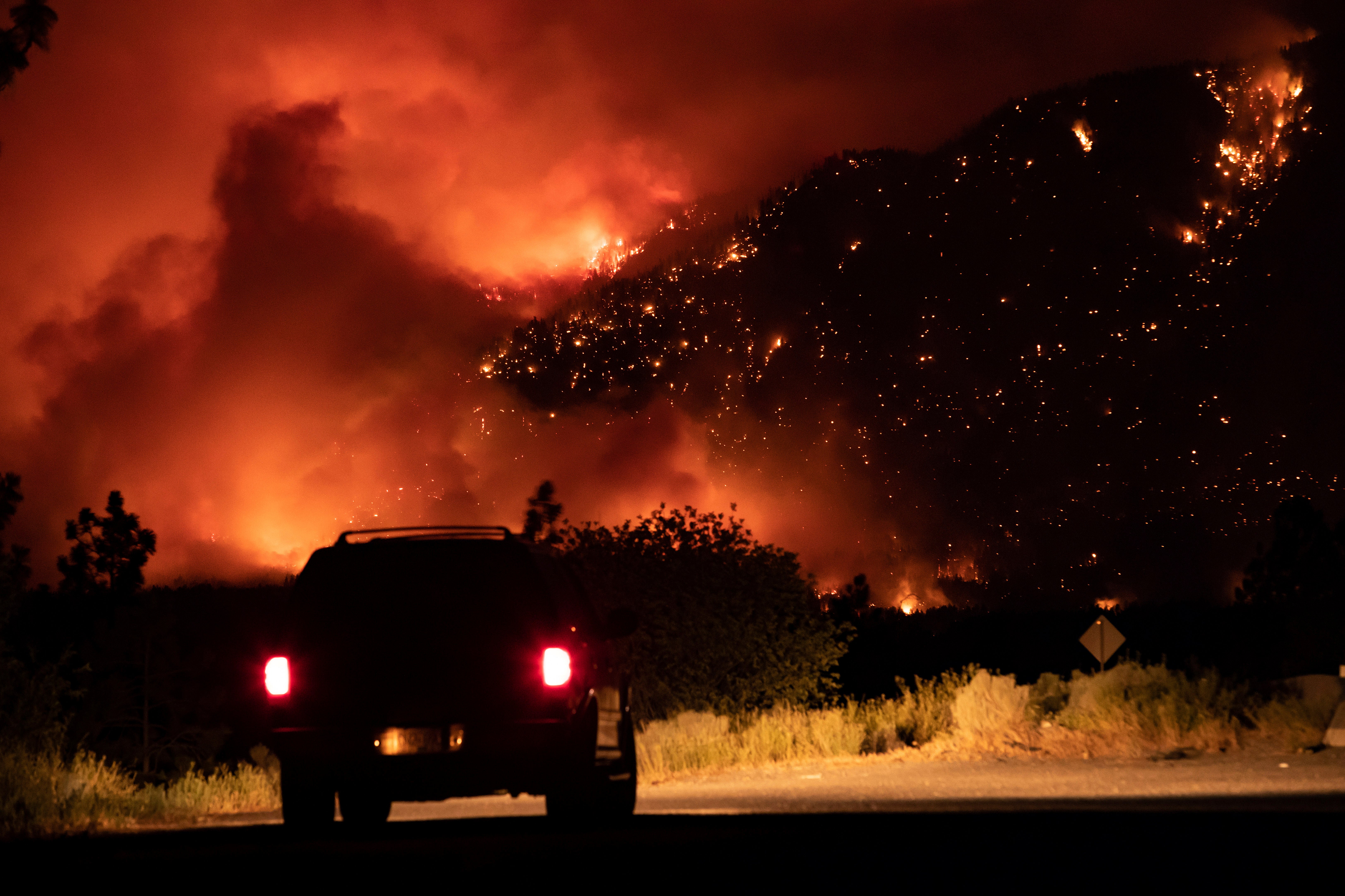 A motorist watches from a pullout on the Trans-Canada Highway as a wildfire burns on the side of a mountain in Lytton, B.C., Thursday, July 1, 2021.