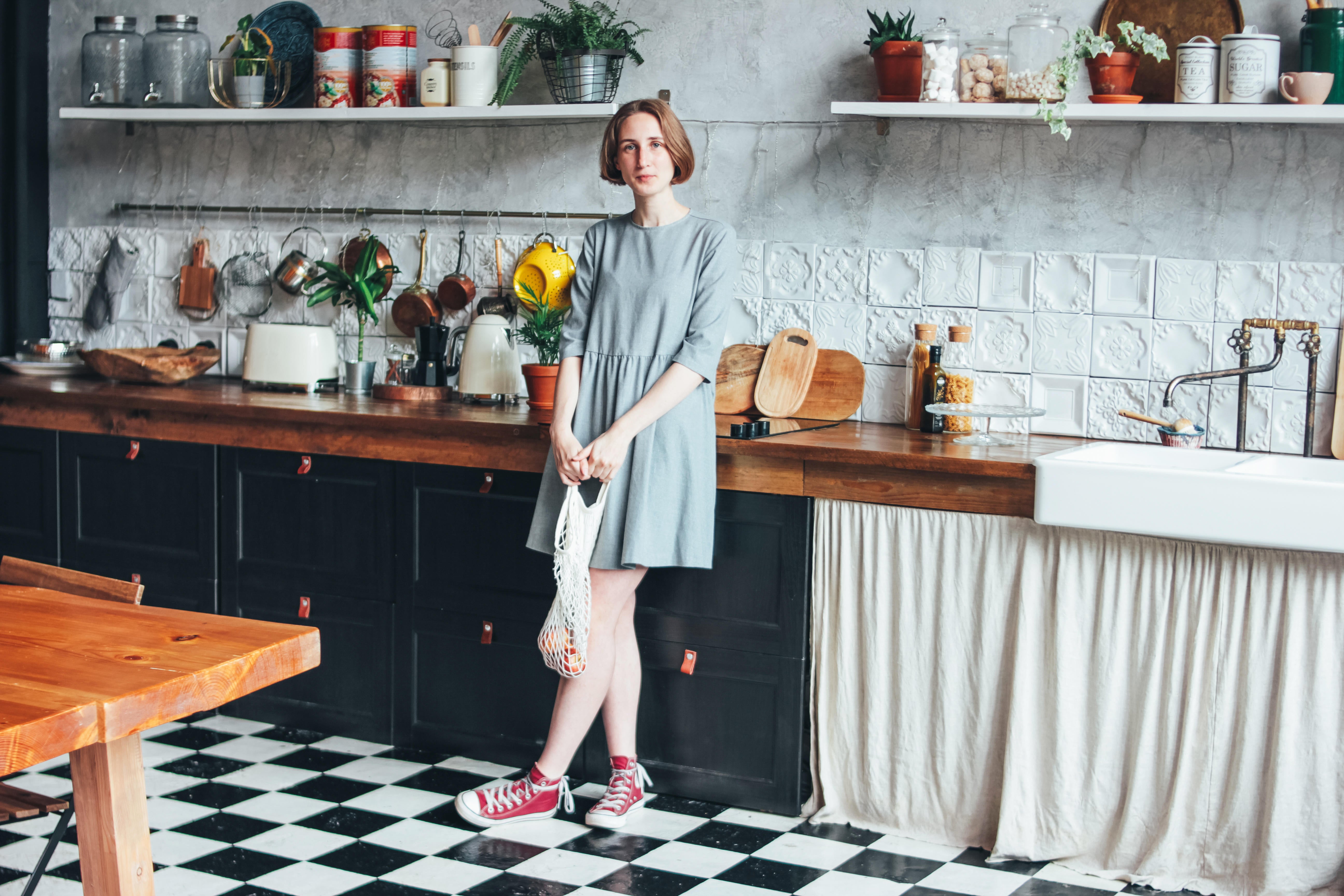 Young woman in grey dress with knitted rag bag string bag shopper in the kitchen, zero waste, slow life