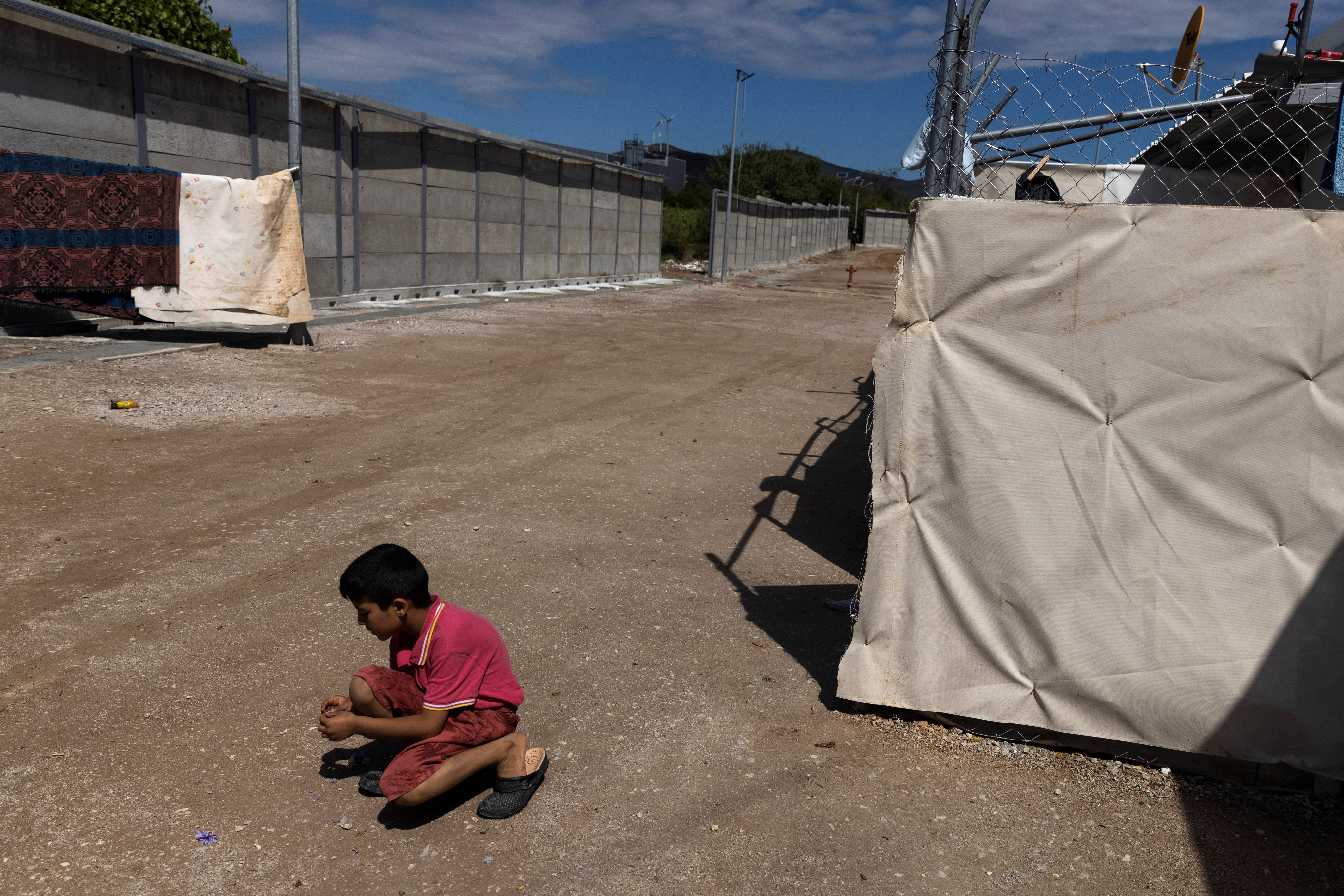 A boy plays next to a newly built concrete wall inside the Ritsona camp for refugees and migrants in Greece