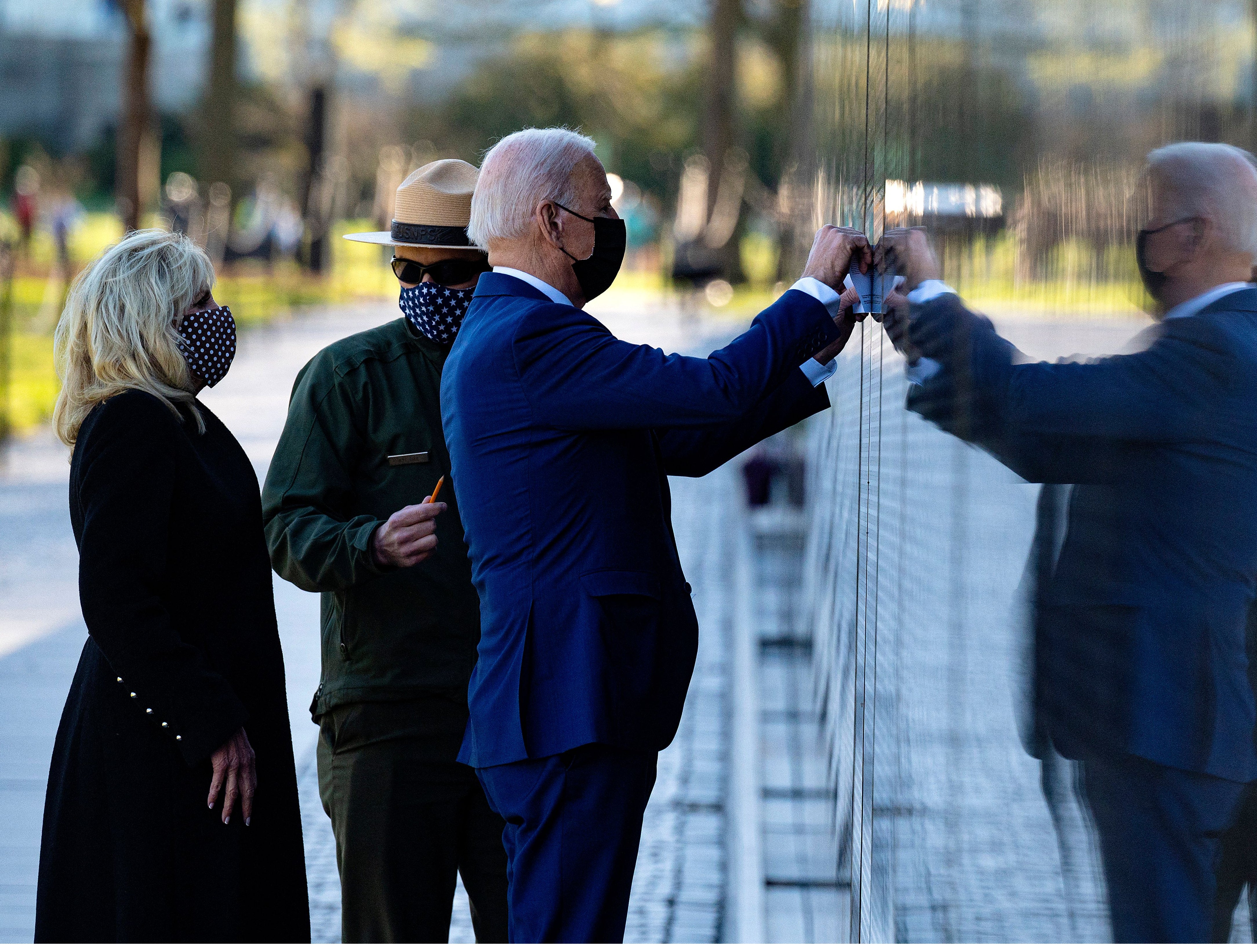 US President Joe Biden, flanked by First Lady Dr Jill Biden, uses paper to trace the name of veteran Dennis F Shine as they visit the Vietnam Veterans Memorial for National Vietnam War Veterans Day in Washington, DC, on March 29, 2021