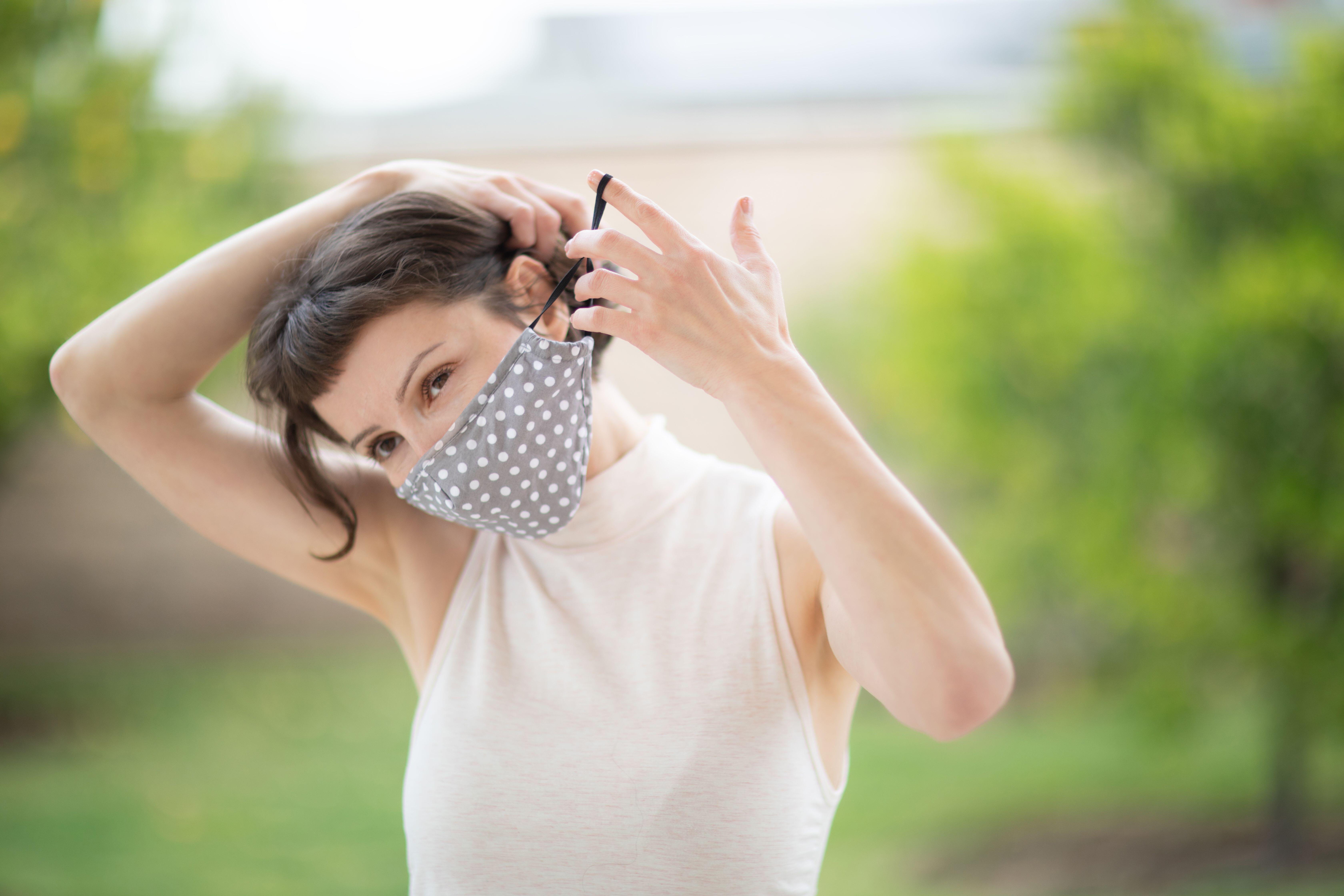 A pretty caucasian woman put on a fabric handmade mask on her face. Due to Covid-19 pandemic, it is recommended that everyone wear face covers while i