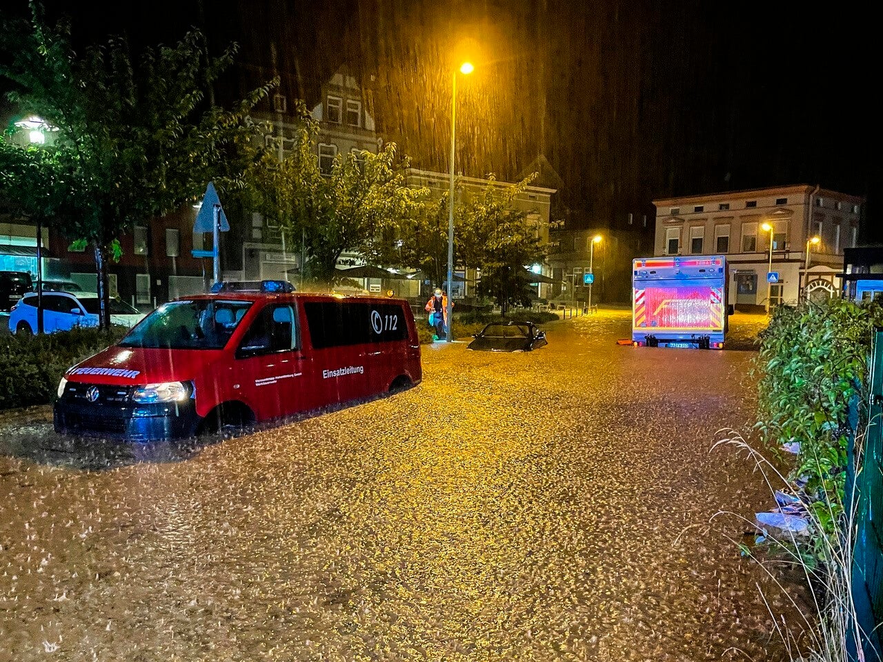 Fire engines and a car are parked on a flooded road in Hagen