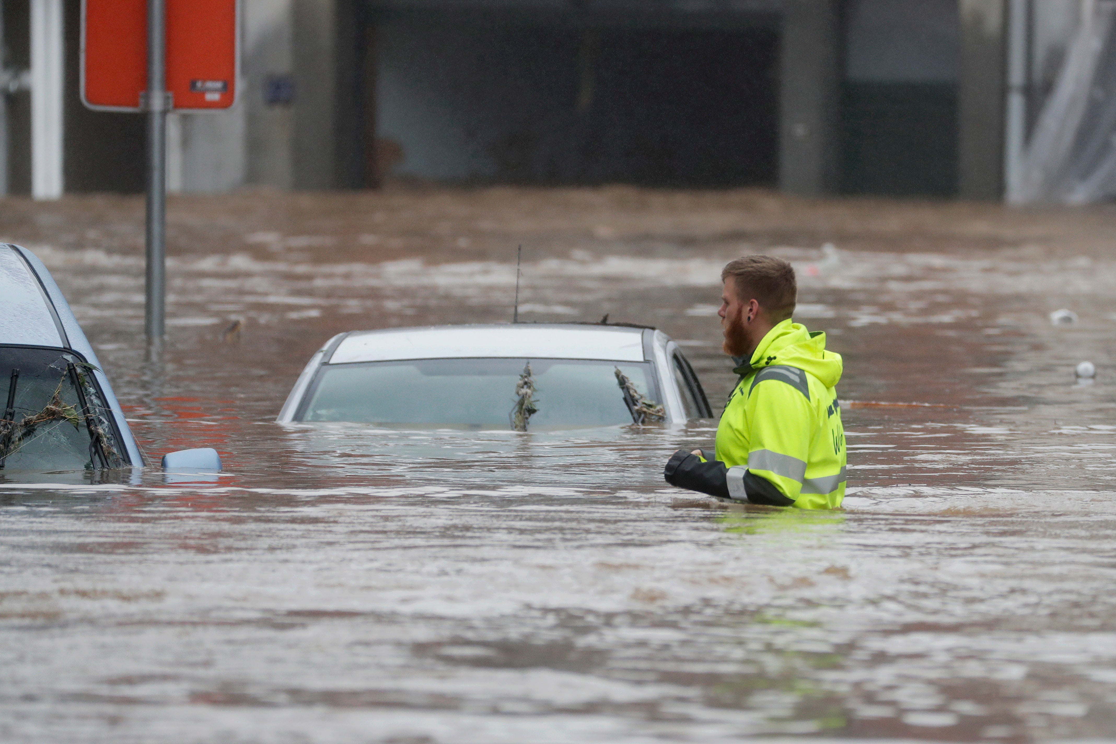 A man wades through the water to reach cars submerged by the heavy rains in Ensival