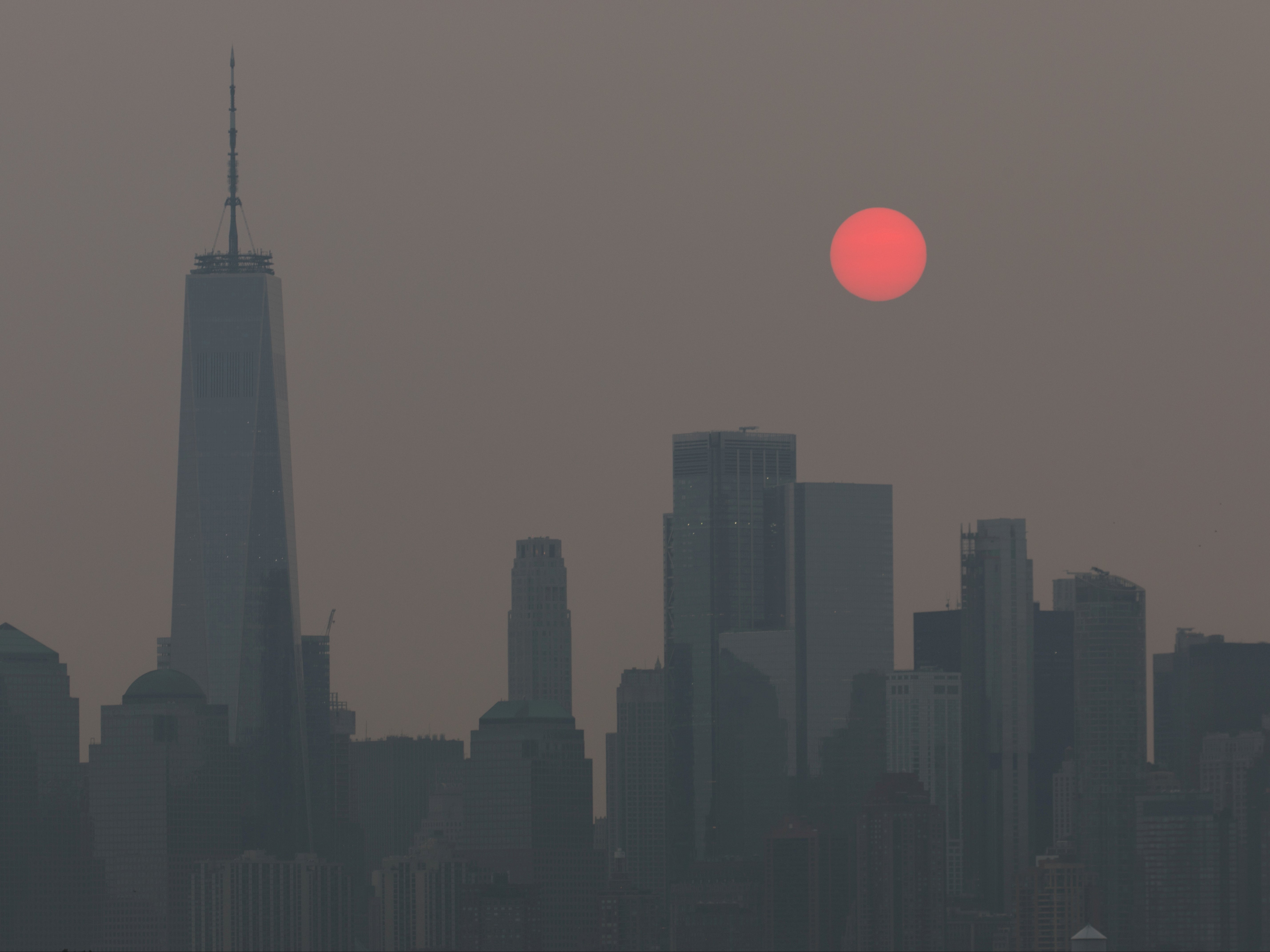 The sun, appearing orange due to smoke haze from forest fires, rises behind the skyline in New York City