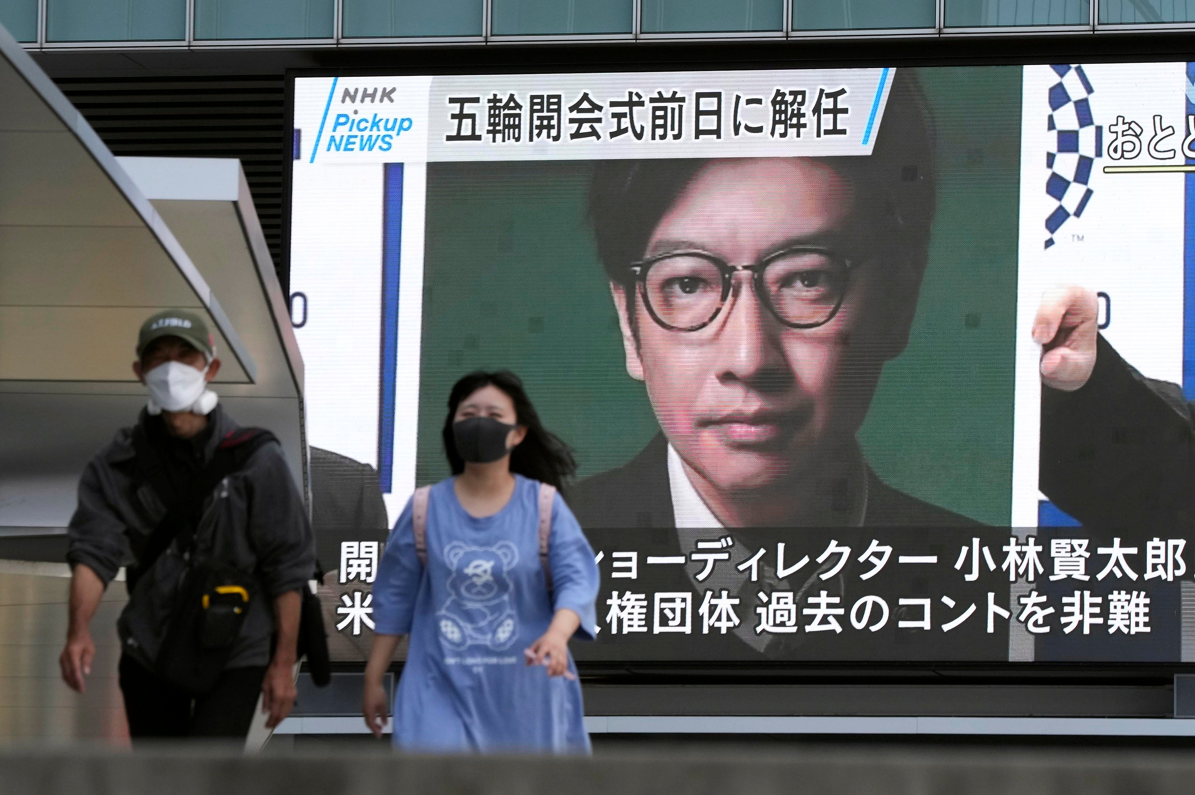 Pedestrians walk past a huge display showing the sacking of Kentaro Kobayashi