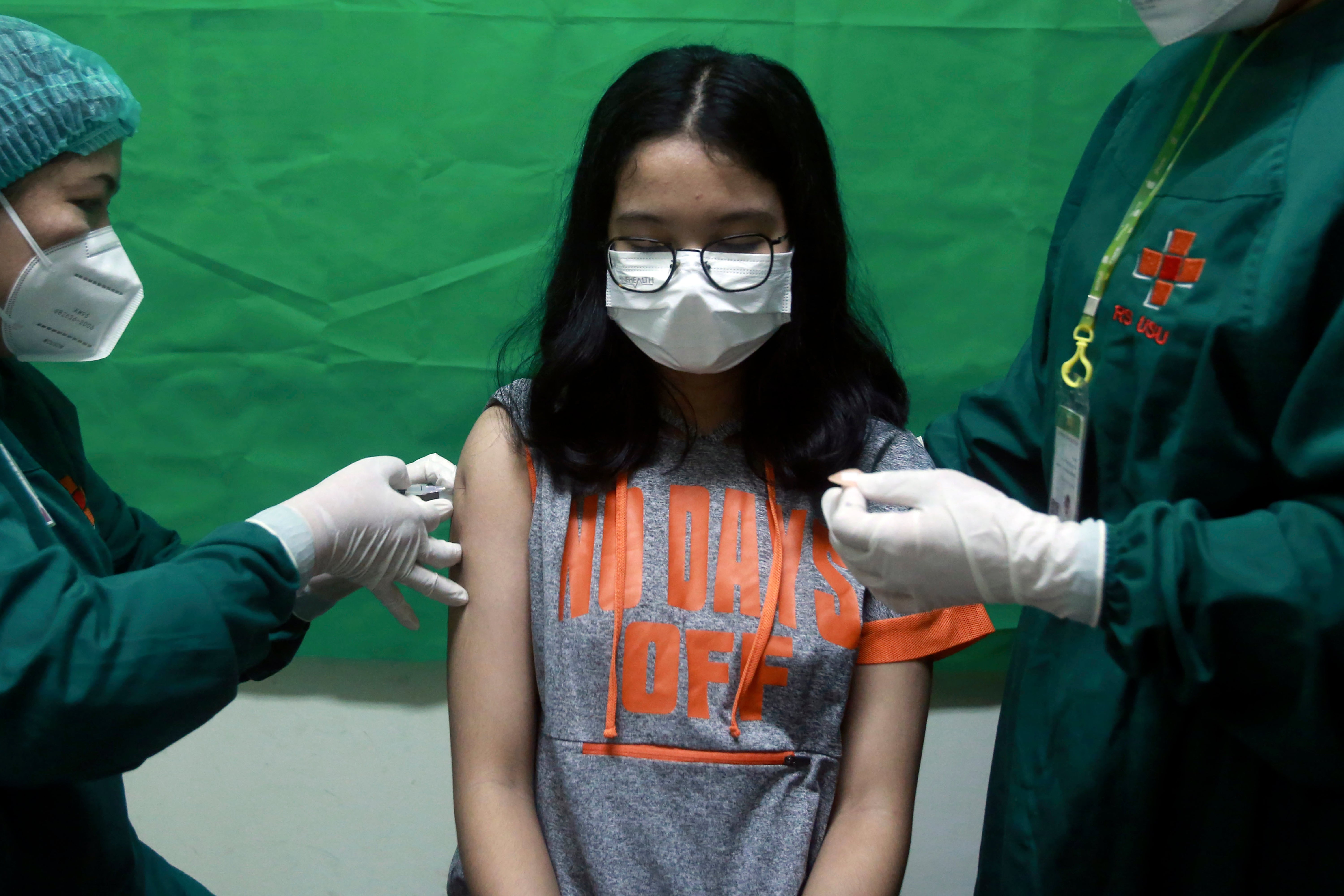 A young girl in Indonesia reacts as medical staff members give her a shot of the Sinovac COVID-19 vaccine during a vaccination campaign for children over twelve years of age