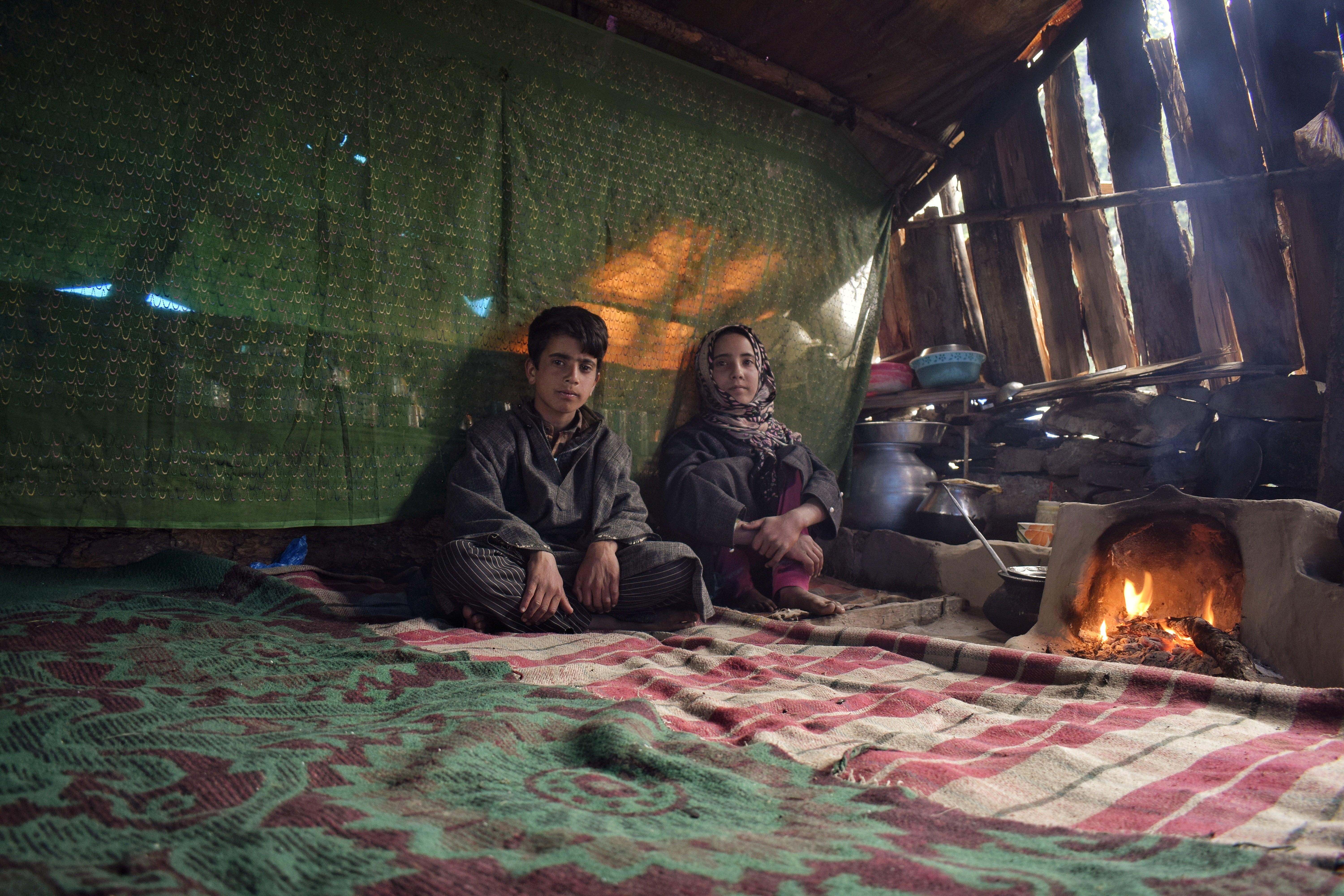 Two siblings belonging to the Gujjar community inside a makeshift hut made of mud and wooden logs