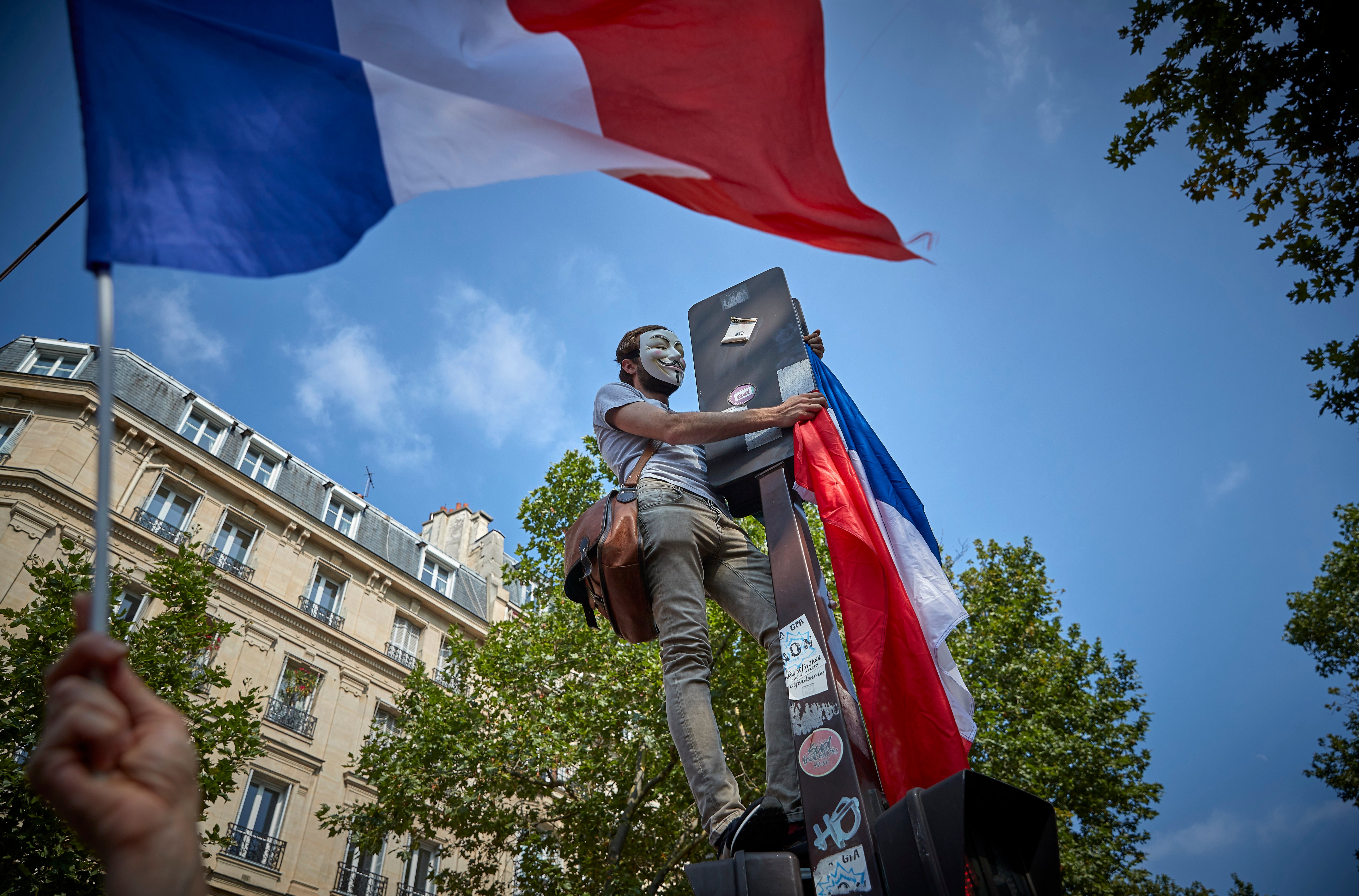 An anti-vaccine protester with a French flag stands on a lamp post as thousands take to the streets of Paris