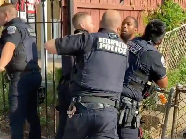 A DC Metropolitan Police Officer pulls back to punch a Black man who is restrained by other officers.