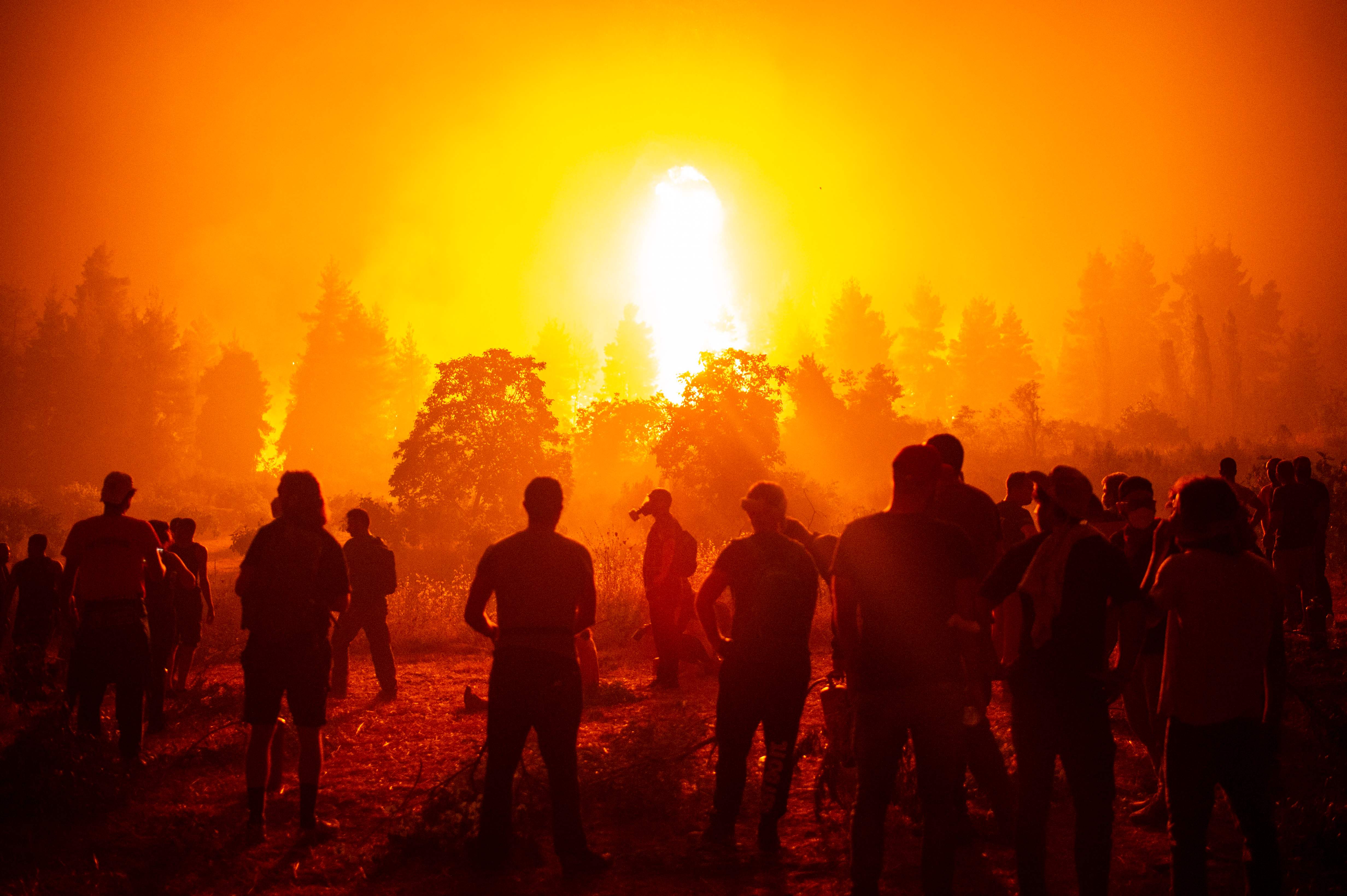 Local youths and volunteers gather in an open field and wait to support firefighters during a wildfire next to the village of Kamatriades, near Istiaia, northern Evia, Greece