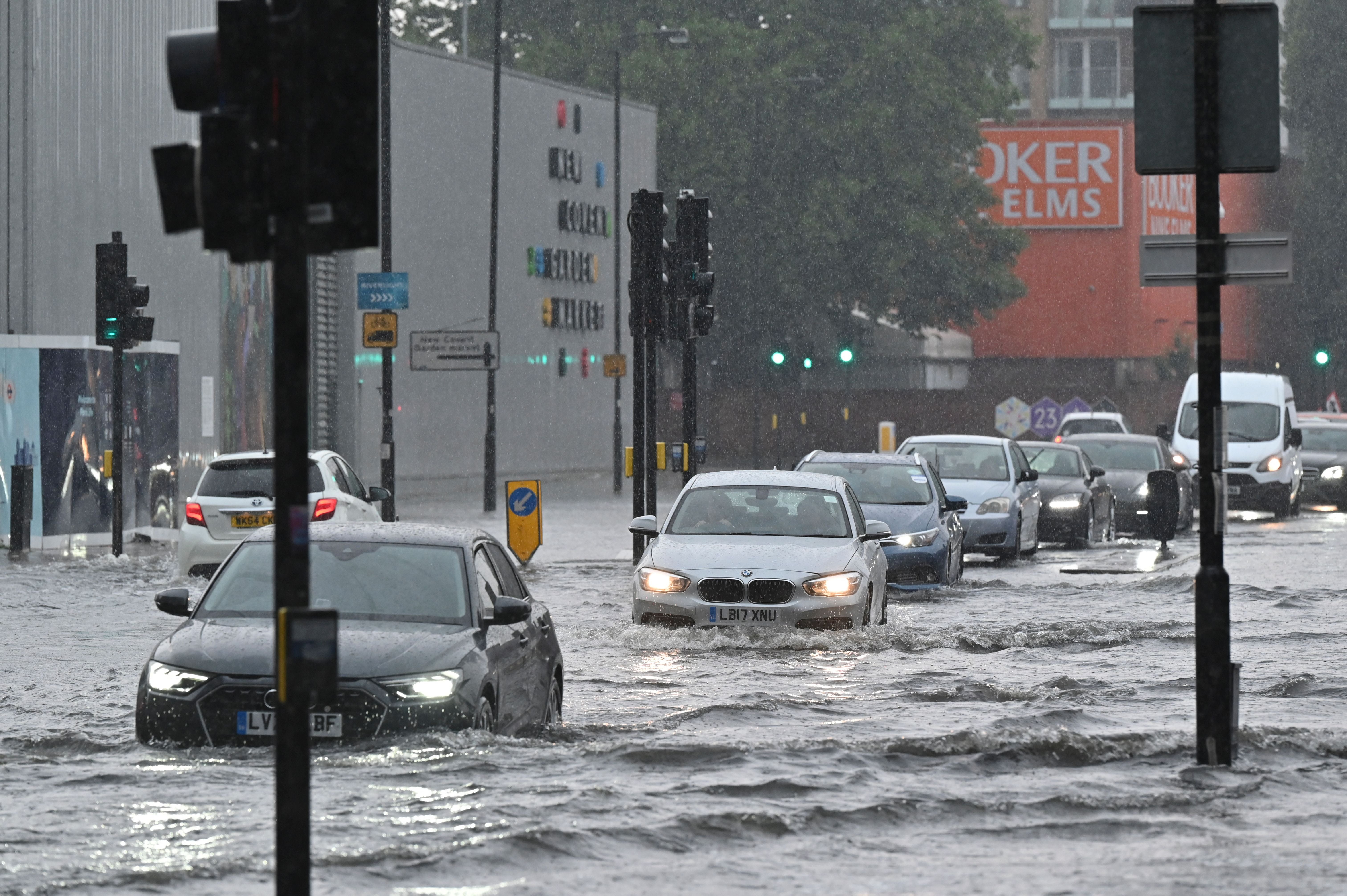 Cars drive through deep water on a flooded road in Nine Elms