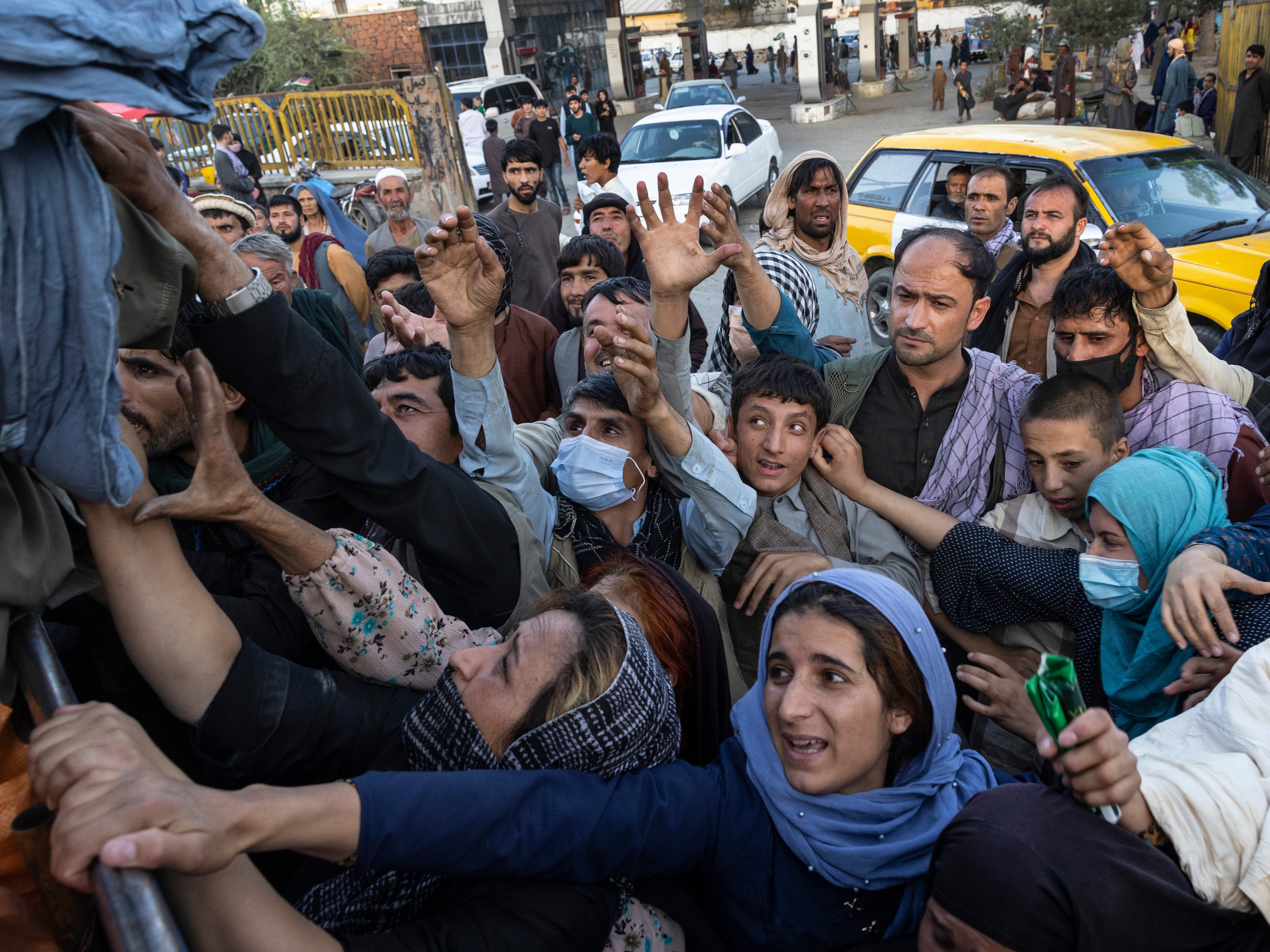 People displaced by Taliban fighting reach out for aid from a local Muslim organisation at a makeship IDP camp in Kabul