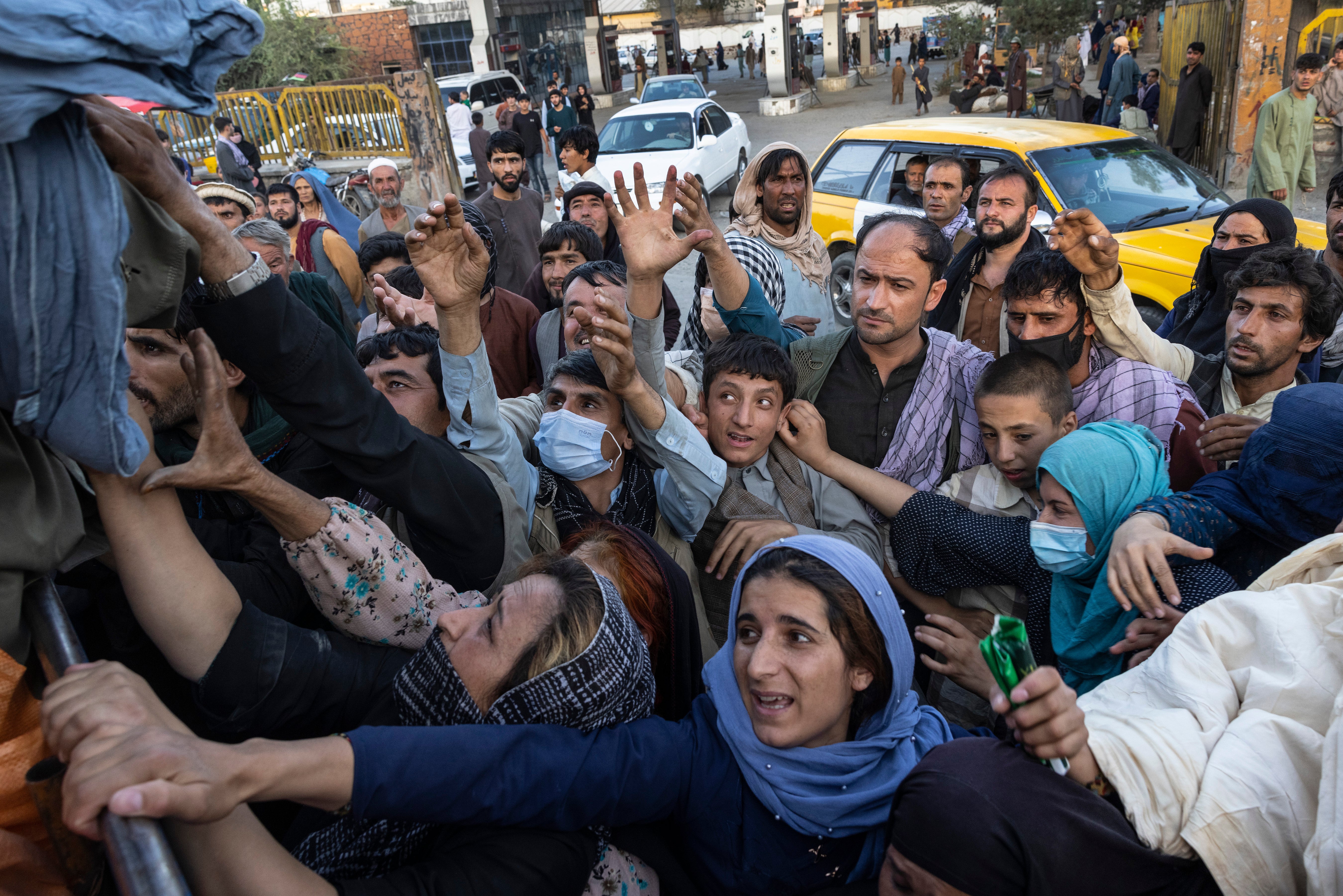 Displaced Afghans reach out for aid from a local Muslim organization at a makeshift IDP camp