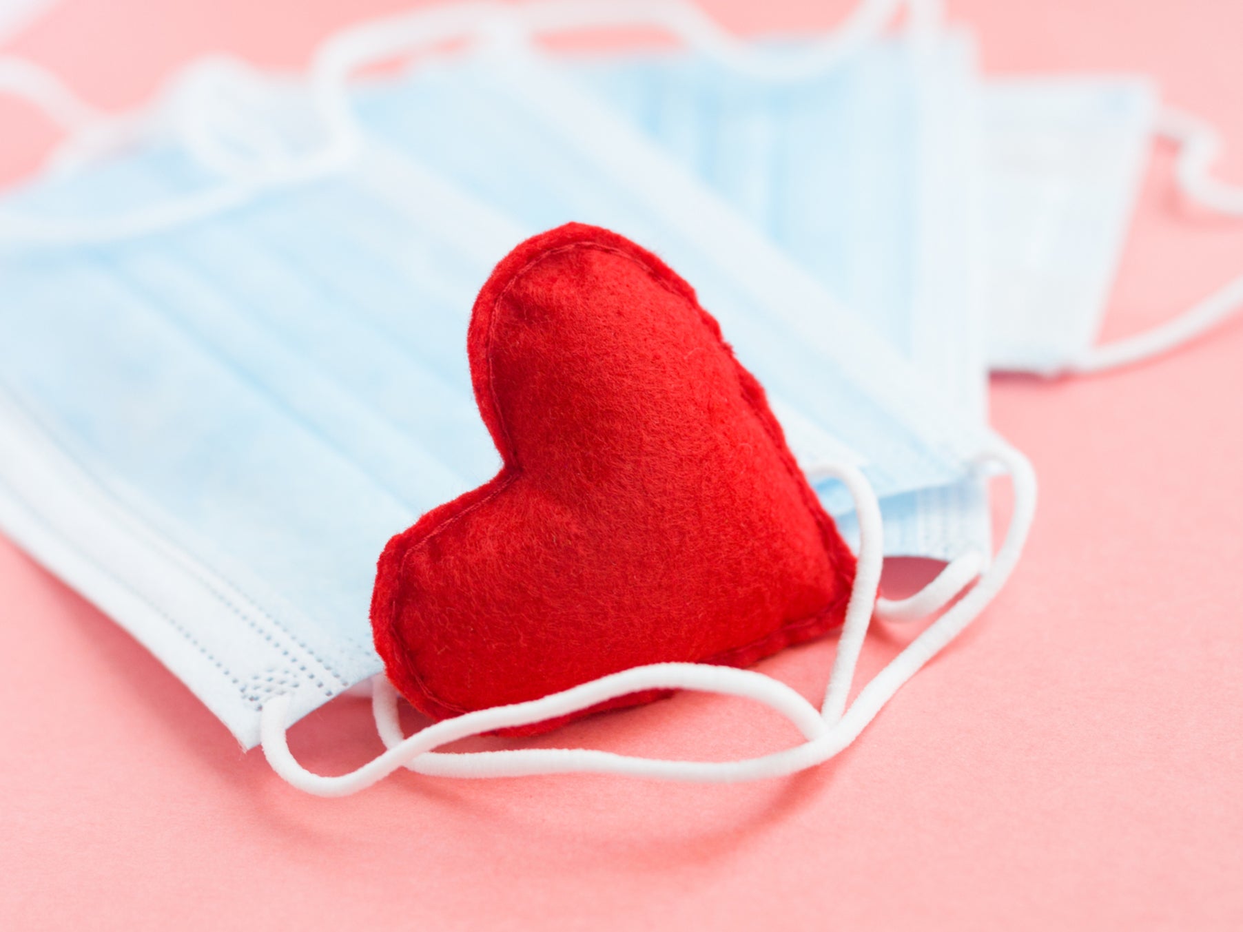 Blue medical face masks and a red heart on a pink background