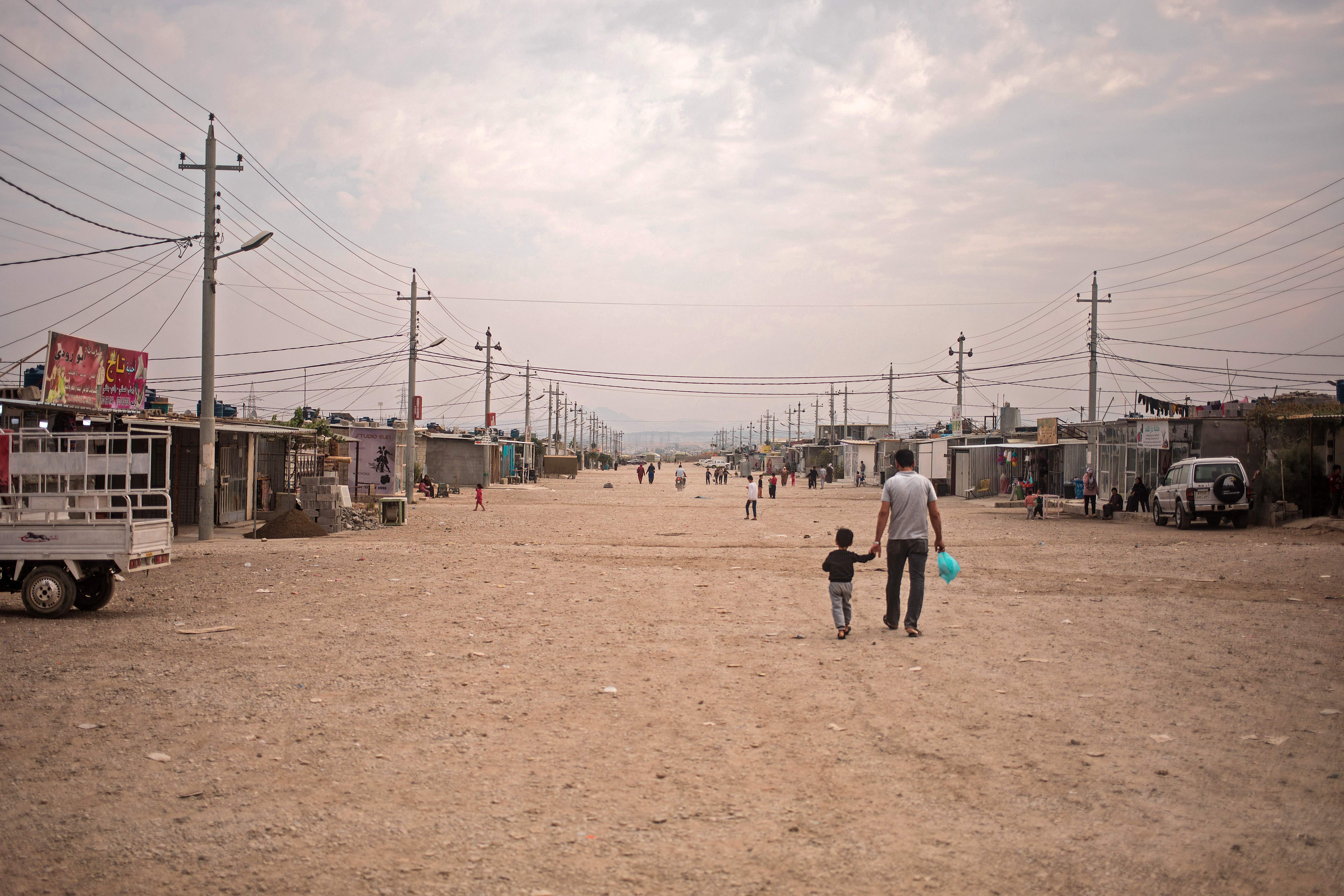 A father and his daughter walk down a central walkway at the Arbat refugee camp