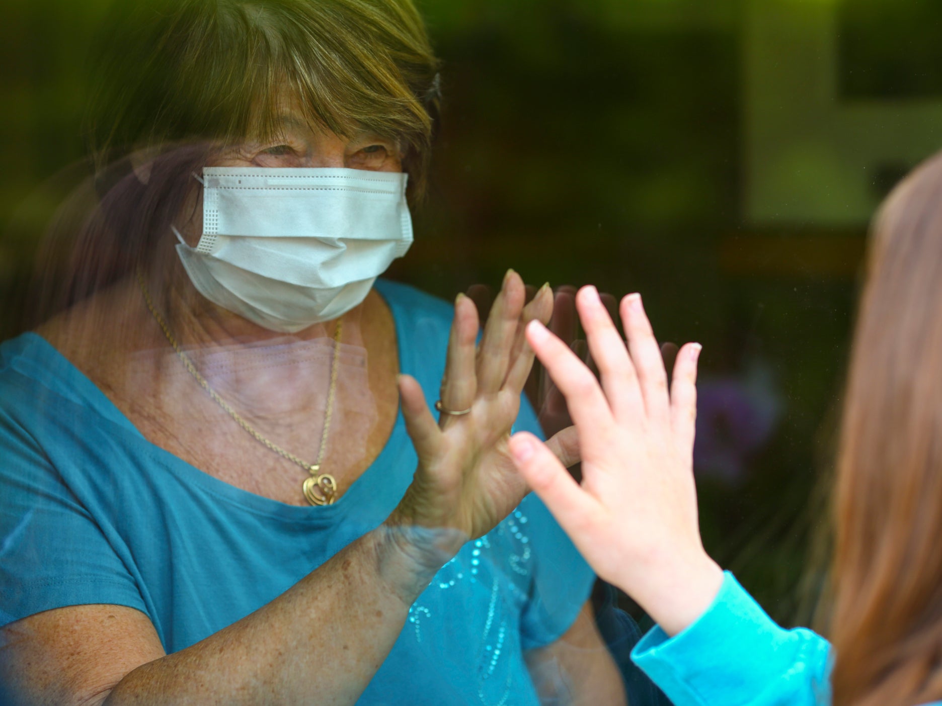 A grandmother and granddaughter touch hands through the window