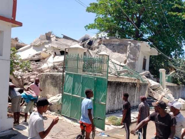 People stand outside the residence of the Catholic bishop after it was damaged by an earthquake in Les Cayes, Haiti