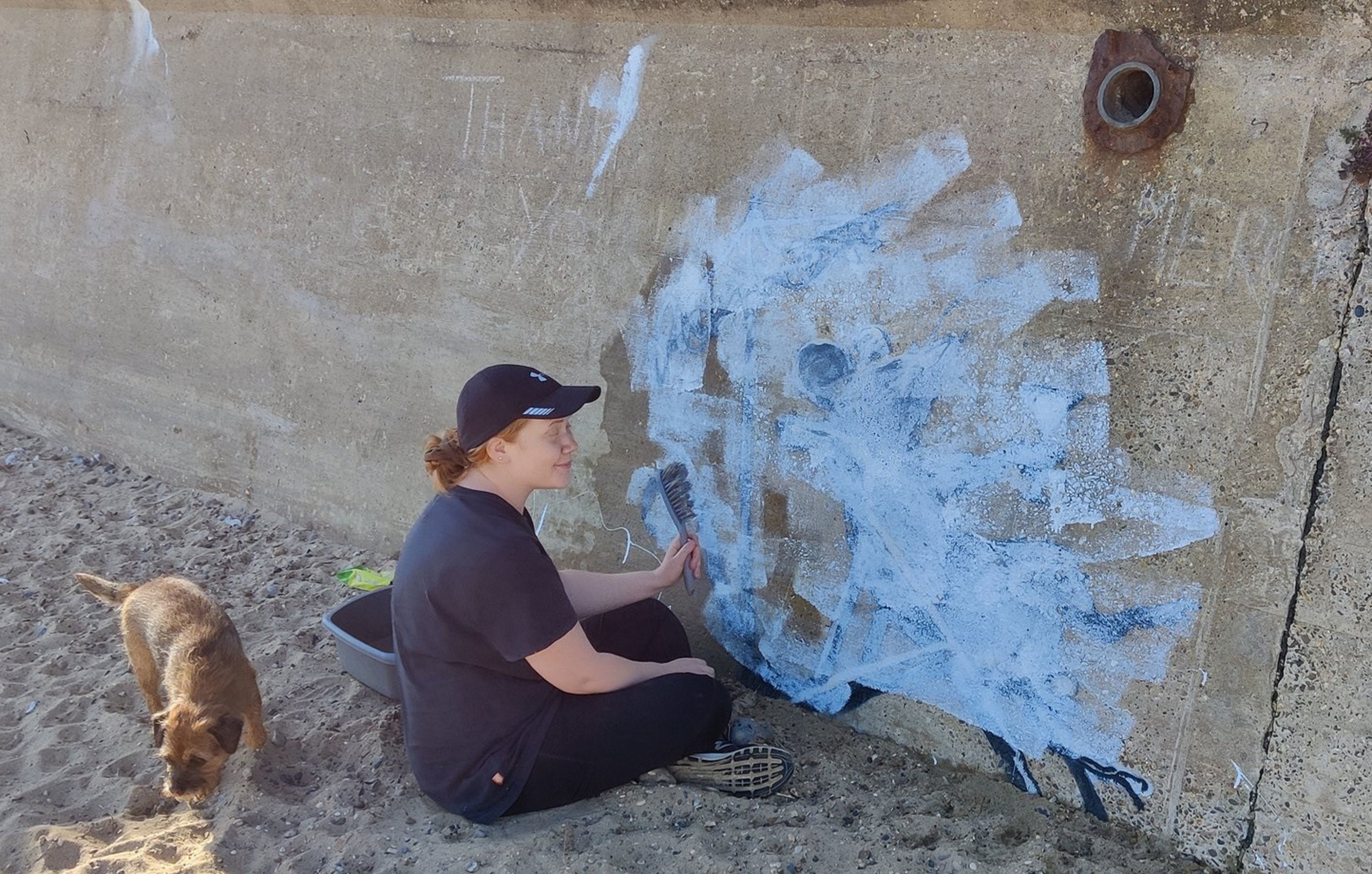 A woman tries to clean the now-defaced mural of a rat in a deckchair