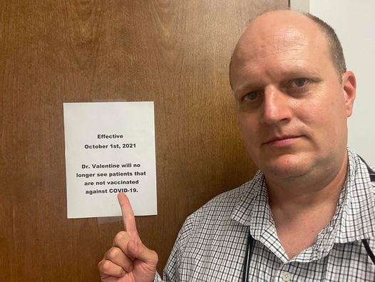 Dr Jason Valentine points to his sign requiring patients to be vaccinated.